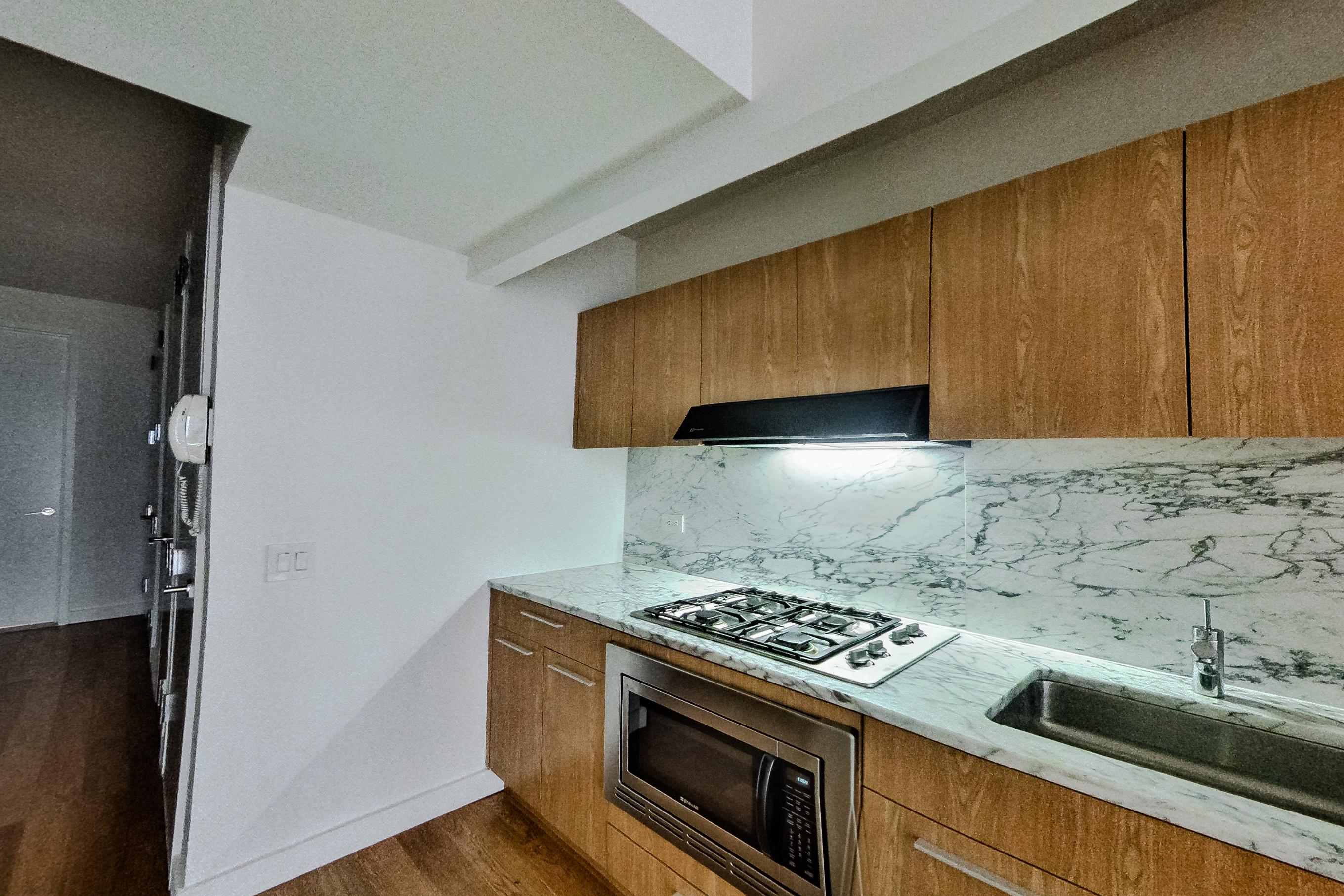 Kitchen with cooktop, dark wood-finish flooring, gas cooktop, light stone countertops, light wood-finish flooring, and stainless steel appliances, Apartment 1805 at Platinum Properties