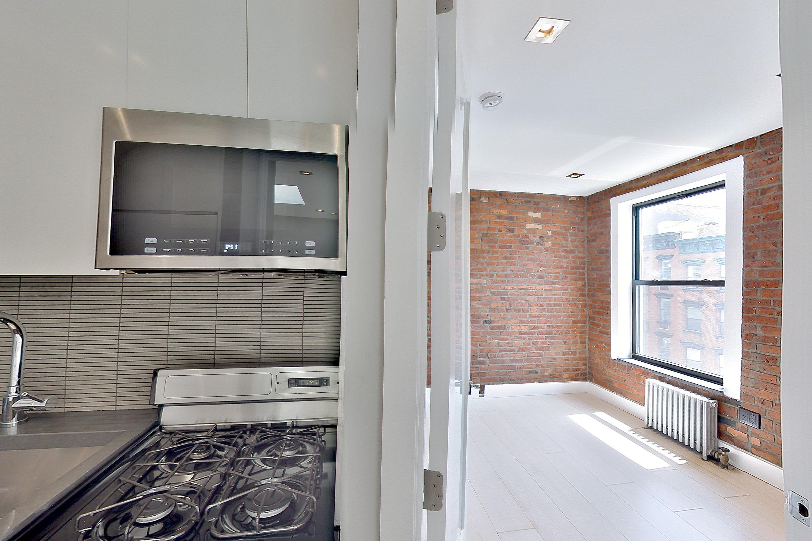 Kitchen with gas range, light wood-finish flooring, oven/range, radiator heat, and stainless steel appliances, Apartment 4 E at Centennial Properties