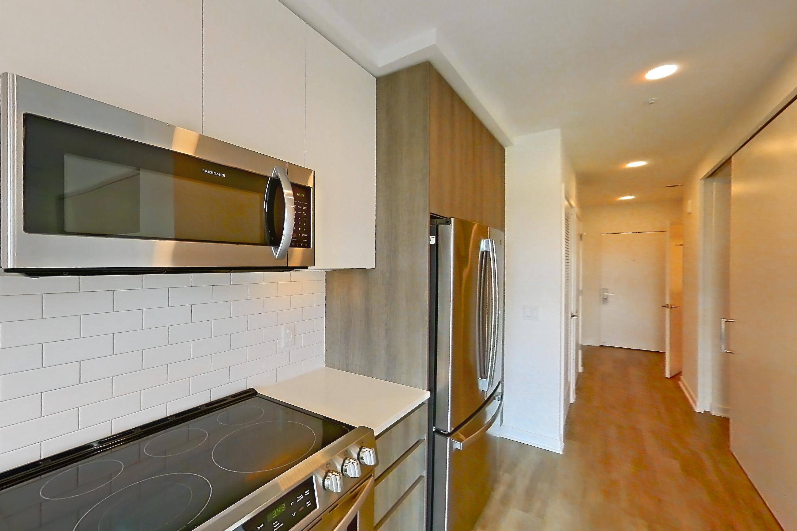 Kitchen with dishwasher, electric range, light countertops, light stone countertops, light wood-finish flooring, microwave, oven/range, refrigerator, and stainless steel appliances, Apartment 3703 at Platform (VA)