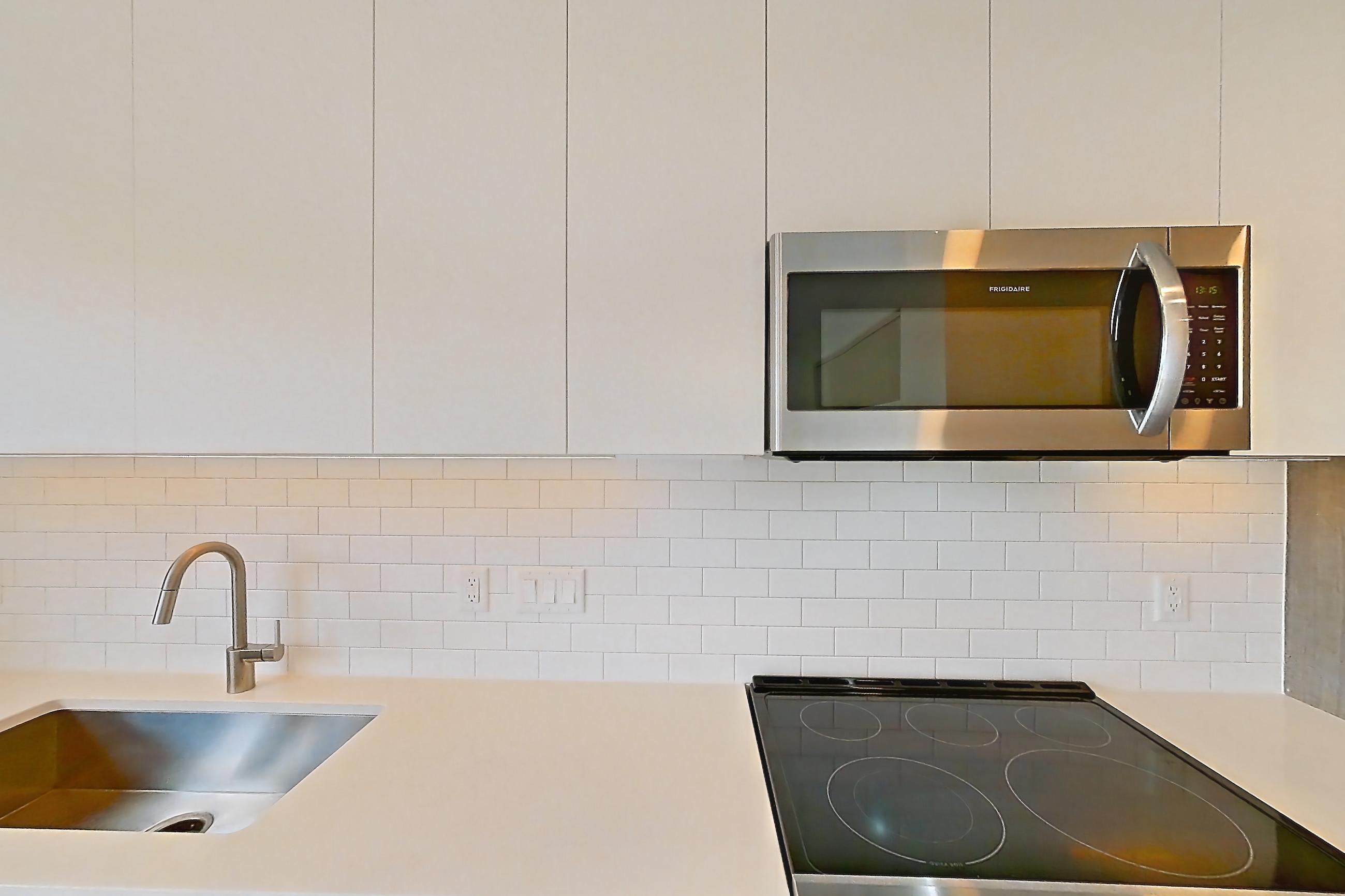Kitchen with dishwasher, electric range, light countertops, light stone countertops, light wood-finish flooring, microwave, oven/range, refrigerator, and stainless steel appliances, Apartment 3703 at Platform (VA)