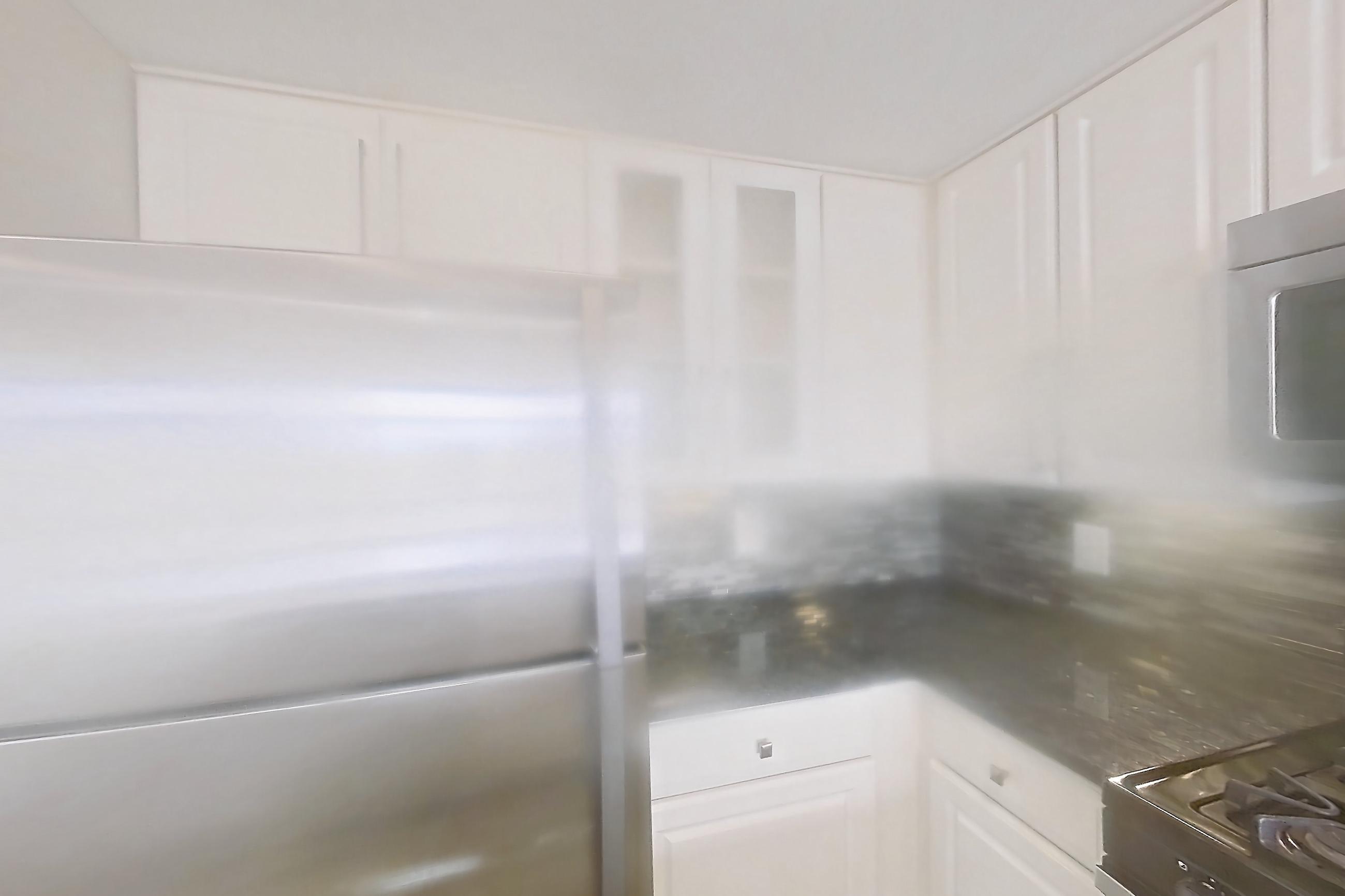 Kitchen with dark stone countertops, gas range, light countertops, light wood-finish flooring, microwave, oven/range, refrigerator, and stainless steel appliances, Apartment 911 at The Barton at Woodley