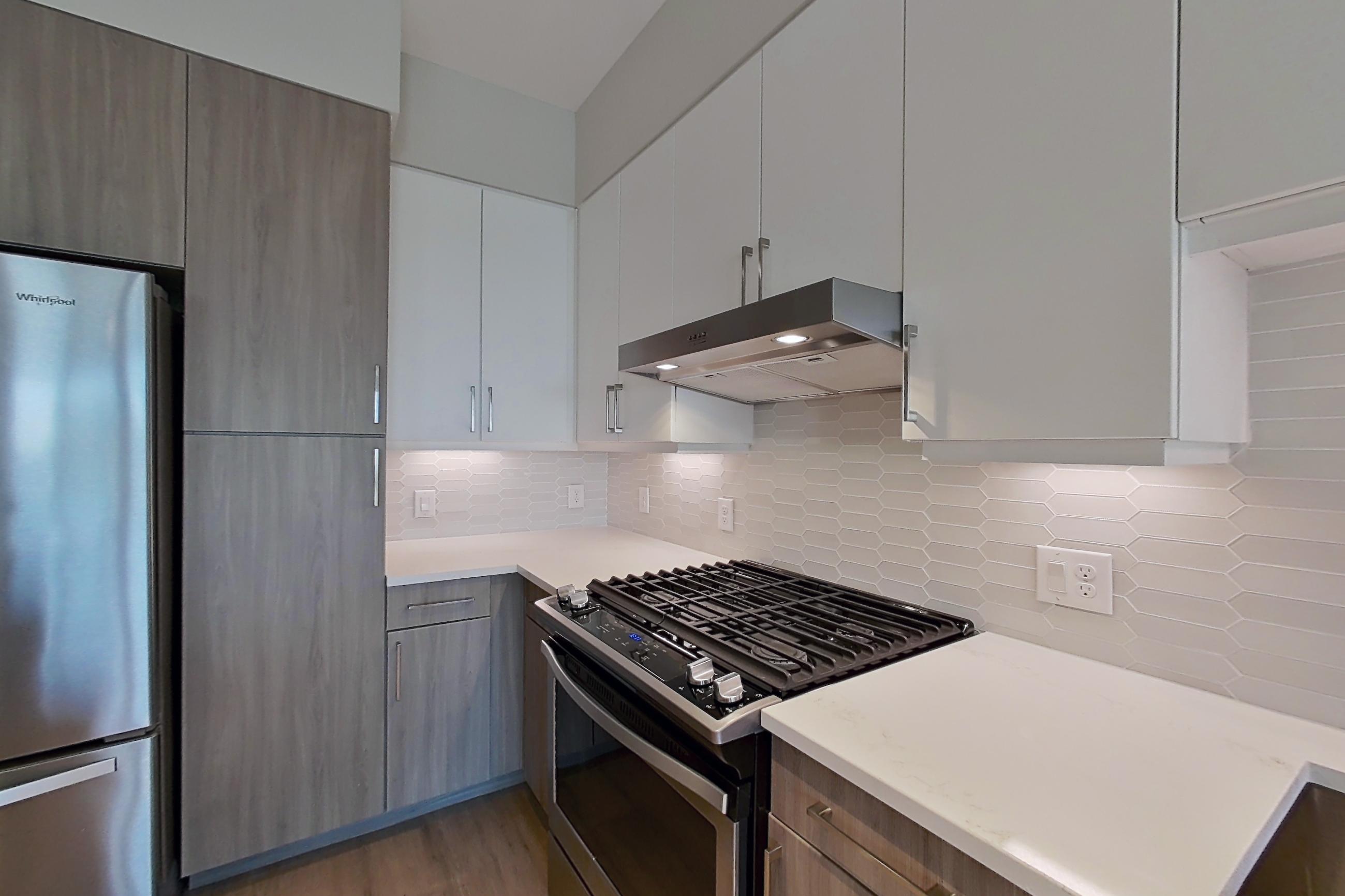 Kitchen with dishwasher, gas range, light countertops, light wood-finish flooring, oven/range, range hood, refrigerator, and stainless steel appliances, Apartment 534 at Montrose at Buffalo Bayou
