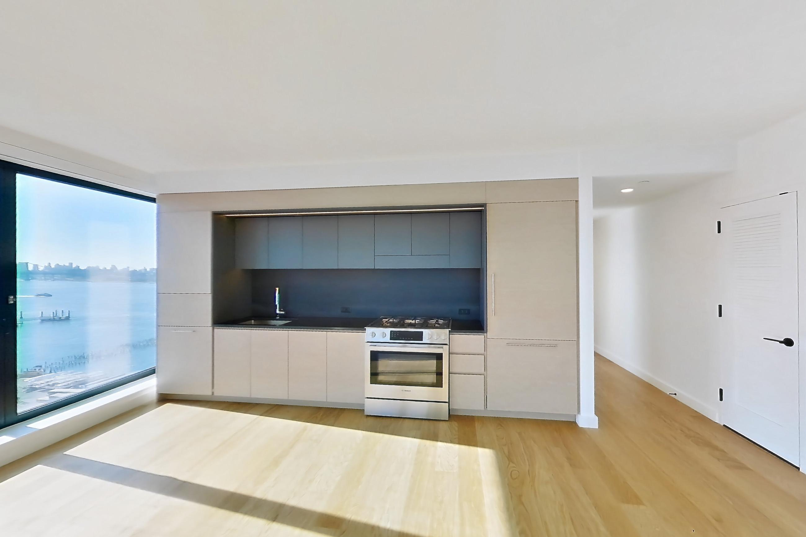 Living room with city view, light wood-finish flooring, oven/range, and stainless steel appliances, Apartment 1-1509 at Eagle + West