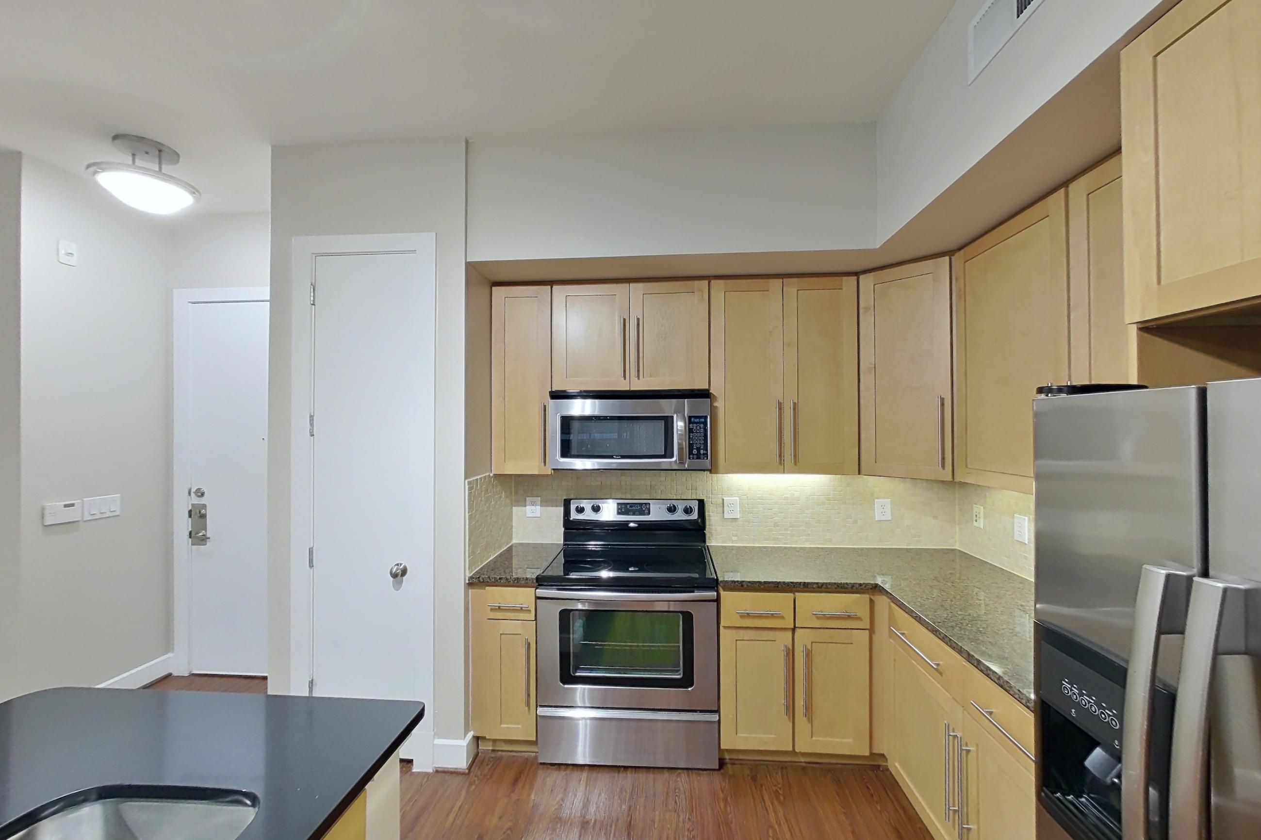 Kitchen with dark countertops, dark stone countertops, dark wood-finish flooring, dishwasher, electric range, light wood-finish flooring, microwave, oven/range, refrigerator, and stainless steel appliances, Apartment 160 at Domain at CityCentre
