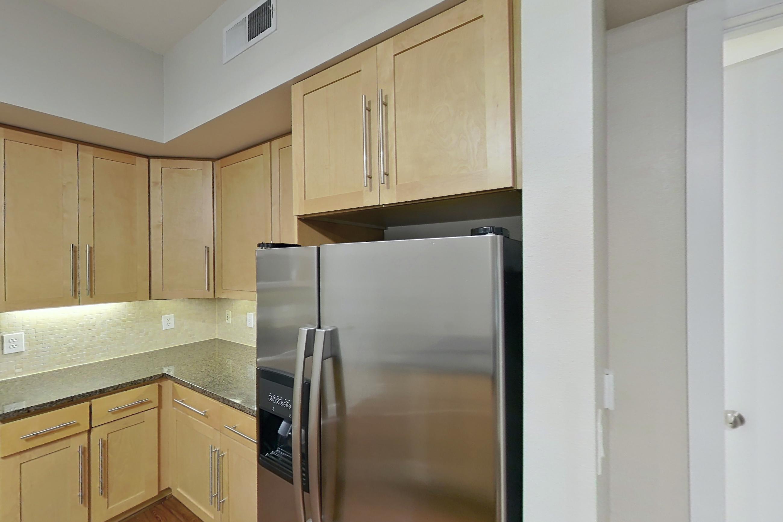 Kitchen with dark countertops, dark stone countertops, dark wood-finish flooring, dishwasher, electric range, light wood-finish flooring, microwave, oven/range, refrigerator, and stainless steel appliances, Apartment 160 at Domain at CityCentre