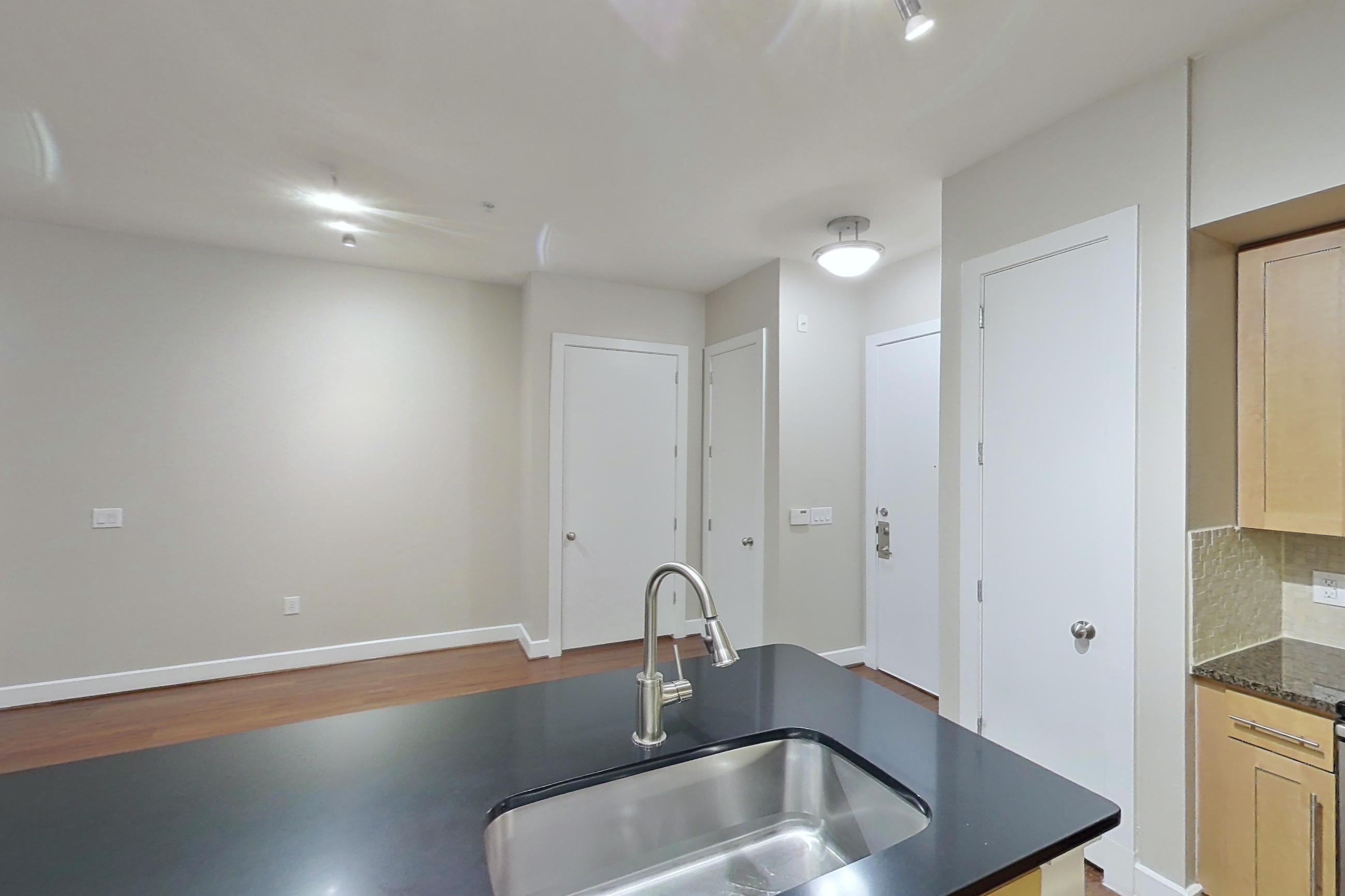 Kitchen with dark countertops, dark stone countertops, dark wood-finish flooring, dishwasher, electric range, light wood-finish flooring, microwave, oven/range, refrigerator, and stainless steel appliances, Apartment 160 at Domain at CityCentre