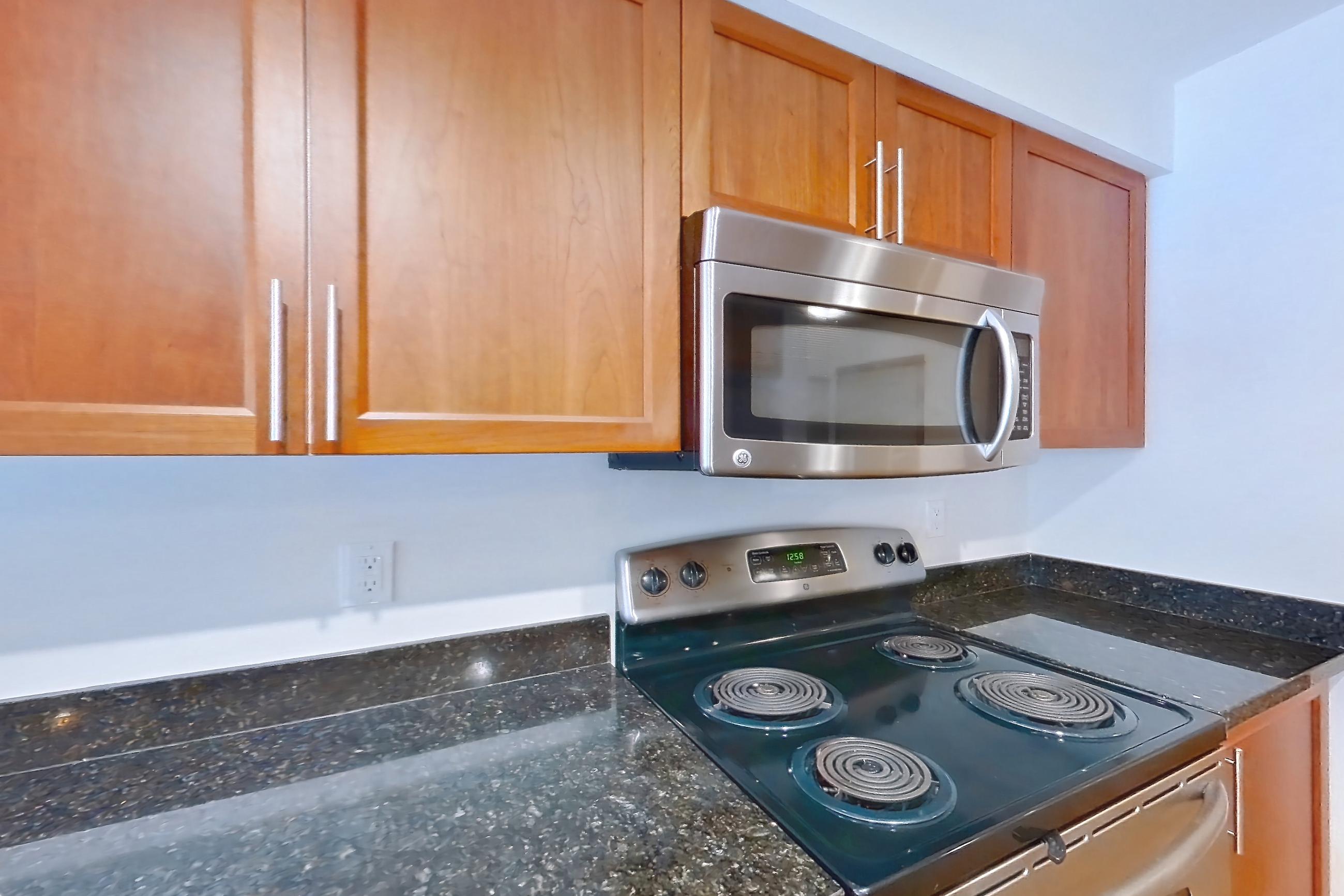 Kitchen with dark stone countertops, electric range, light wood-finish flooring, oven/range, and stainless steel appliances, Apartment B245 at 77 Central