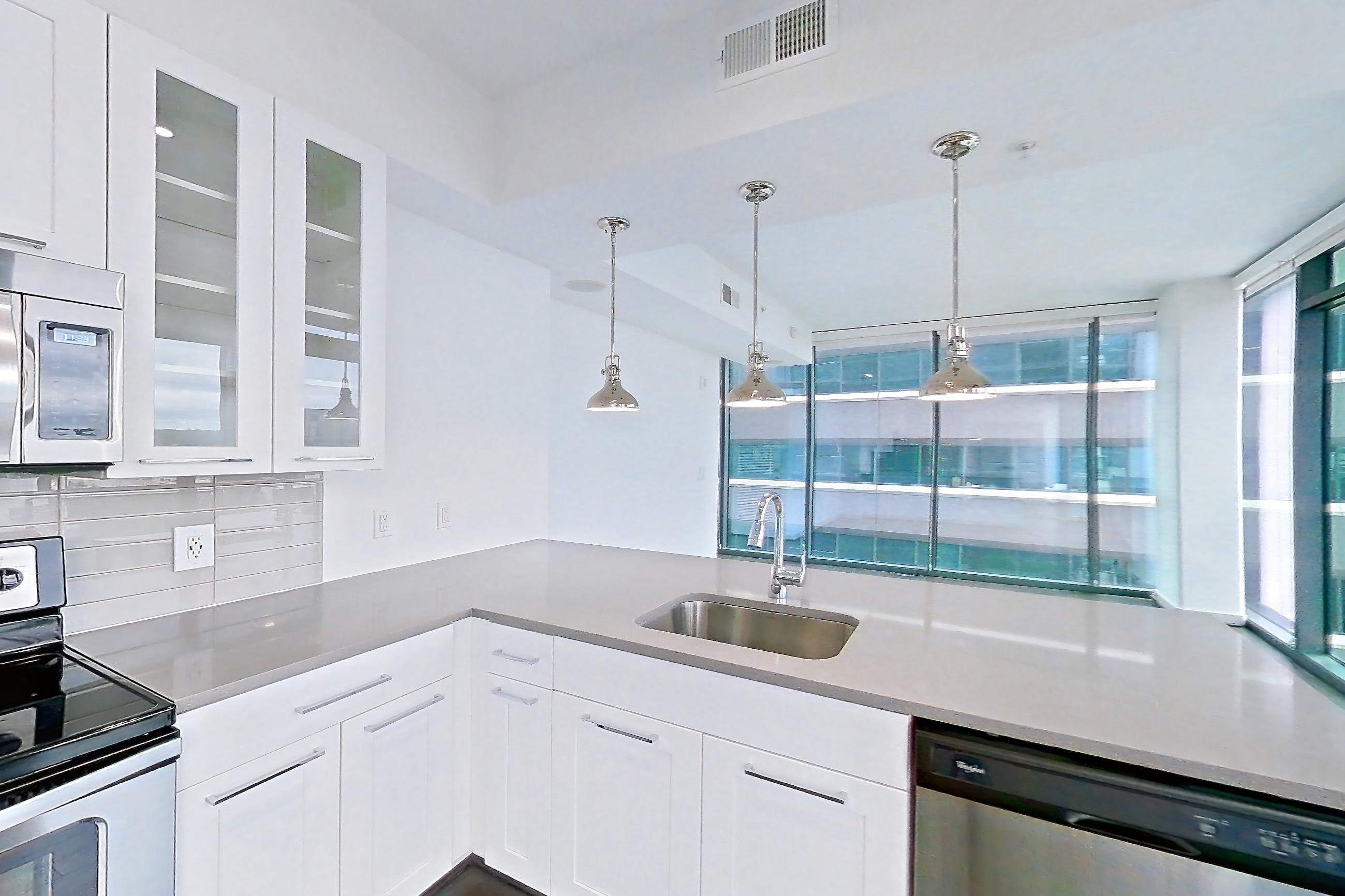 Kitchen with dark wood-finish flooring, dishwasher, electric range, light countertops, microwave, oven/range, refrigerator, stainless steel appliances, water & ice dispenser, and white appliances, Apartment 0915 at Cyan on Peachtree
