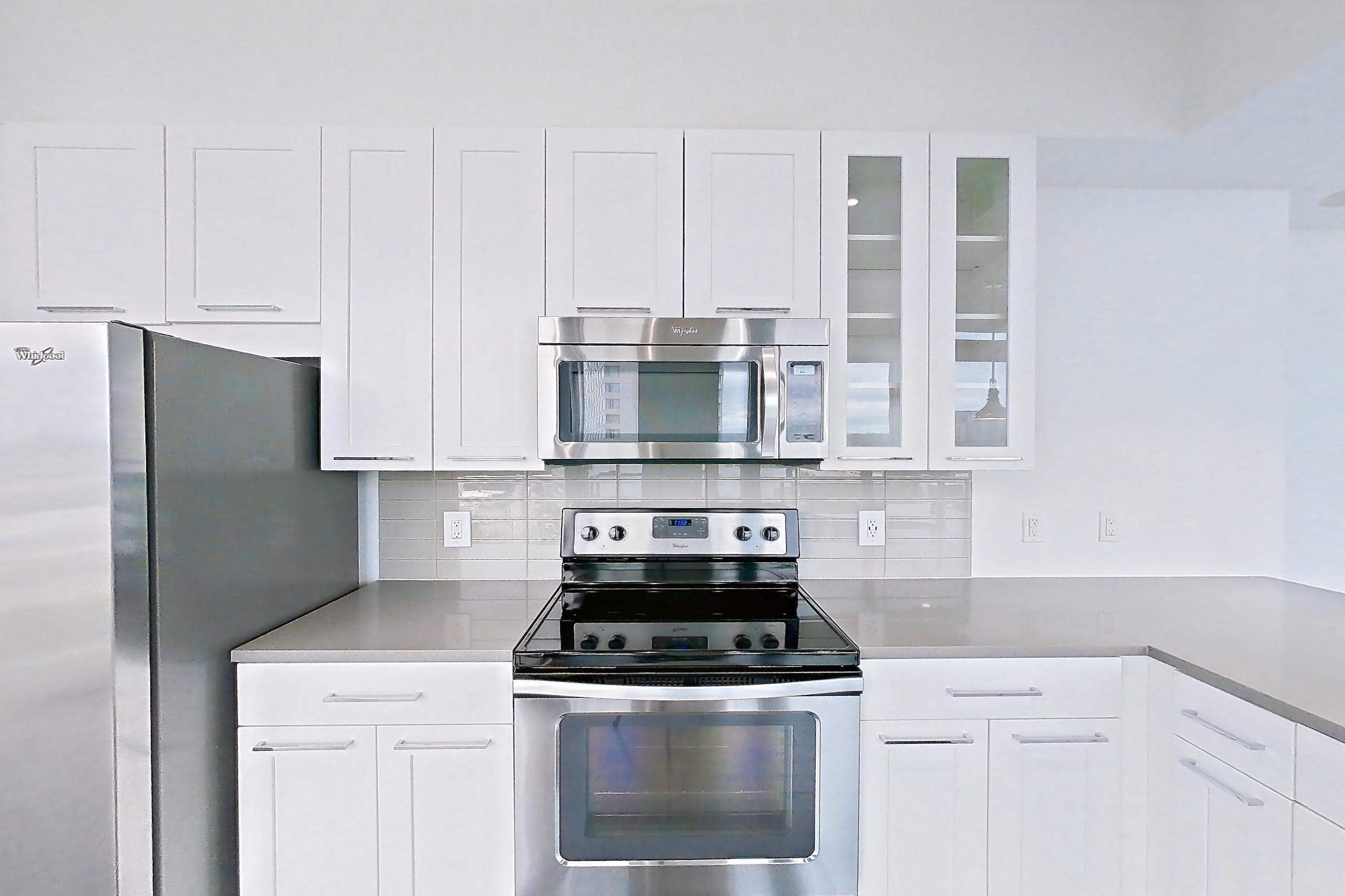 Kitchen with dark wood-finish flooring, dishwasher, electric range, light countertops, microwave, oven/range, refrigerator, stainless steel appliances, water & ice dispenser, and white appliances, Apartment 0915 at Cyan on Peachtree
