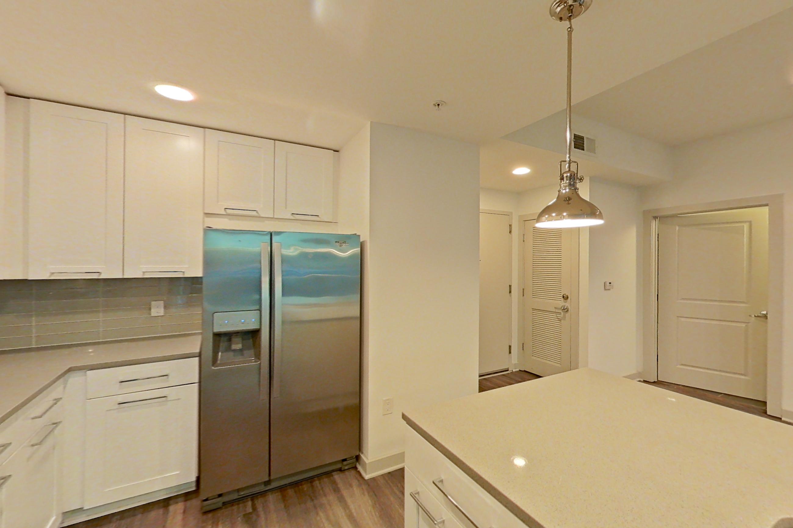 Kitchen with dark wood-finish flooring, dishwasher, electric range, light countertops, oven/range, refrigerator, stainless steel appliances, and water & ice dispenser, Apartment 0206 at Cyan on Peachtree