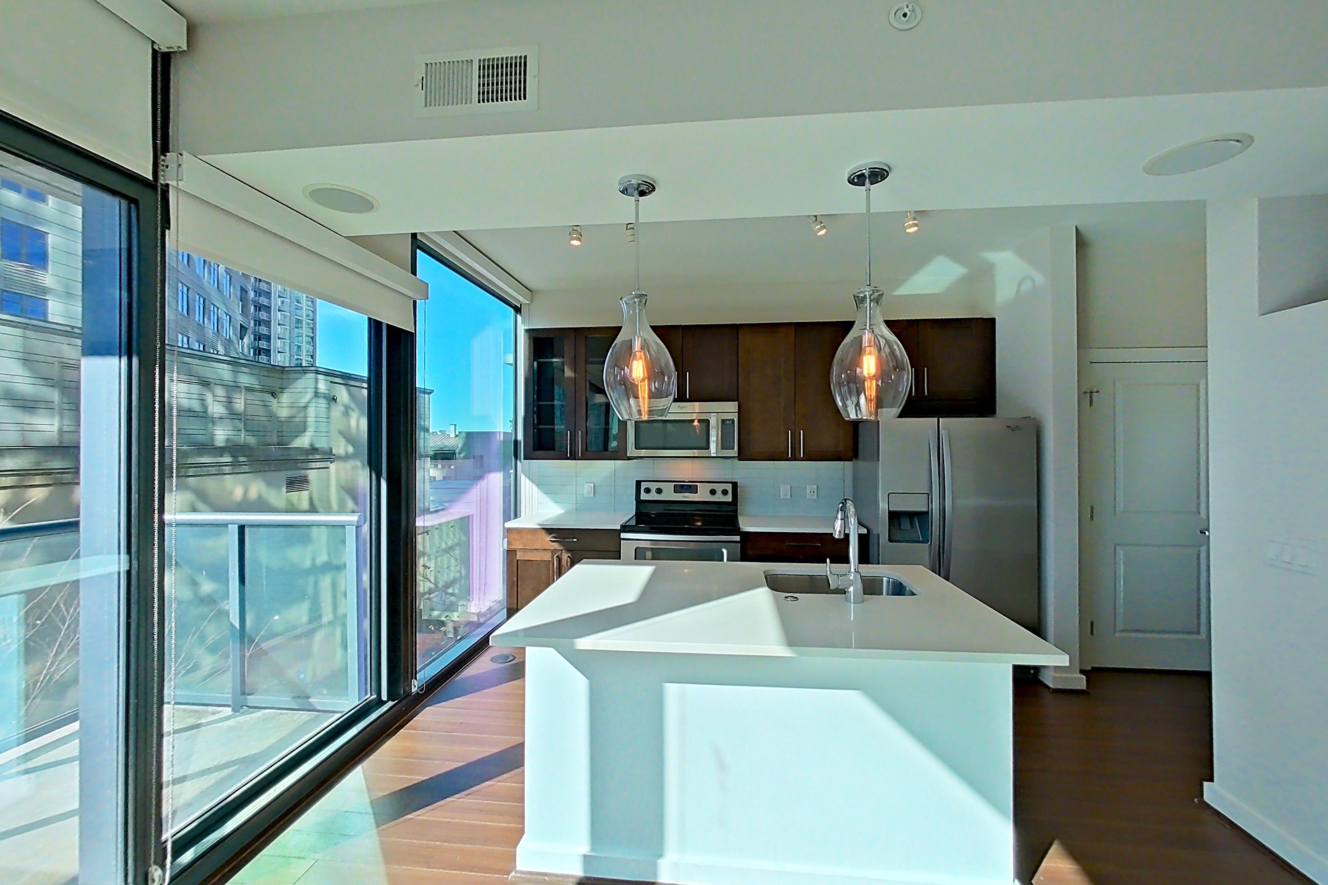 Living room with dark wood-finish flooring, electric range, kitchen island, light countertops, oven/range, refrigerator, stainless steel appliances, and water & ice dispenser, Apartment 0608 at Cyan on Peachtree