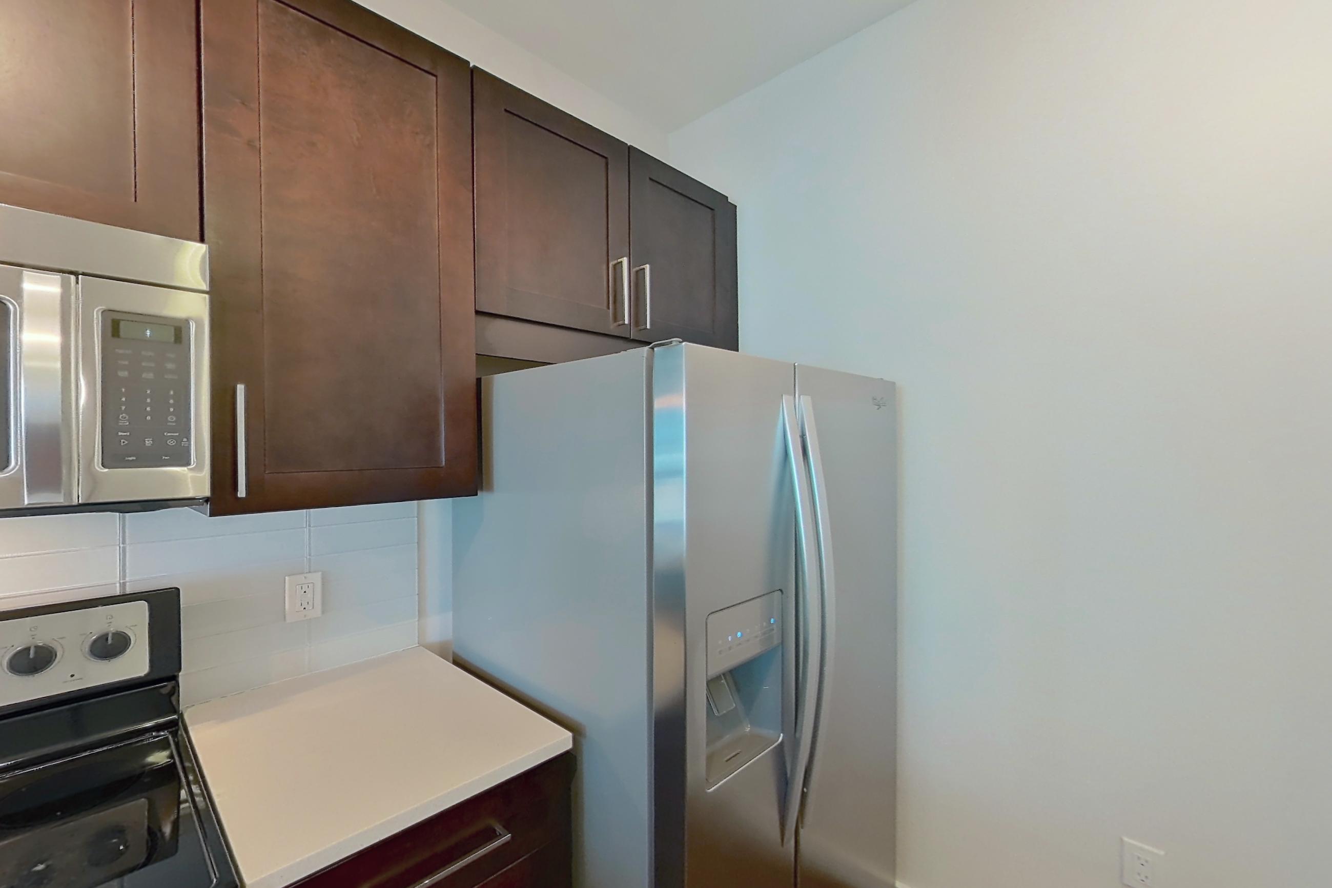 Kitchen with dark wood-finish flooring, dishwasher, electric range, light countertops, microwave, oven/range, refrigerator, stainless steel appliances, and water & ice dispenser, Apartment 1011 at Cyan on Peachtree