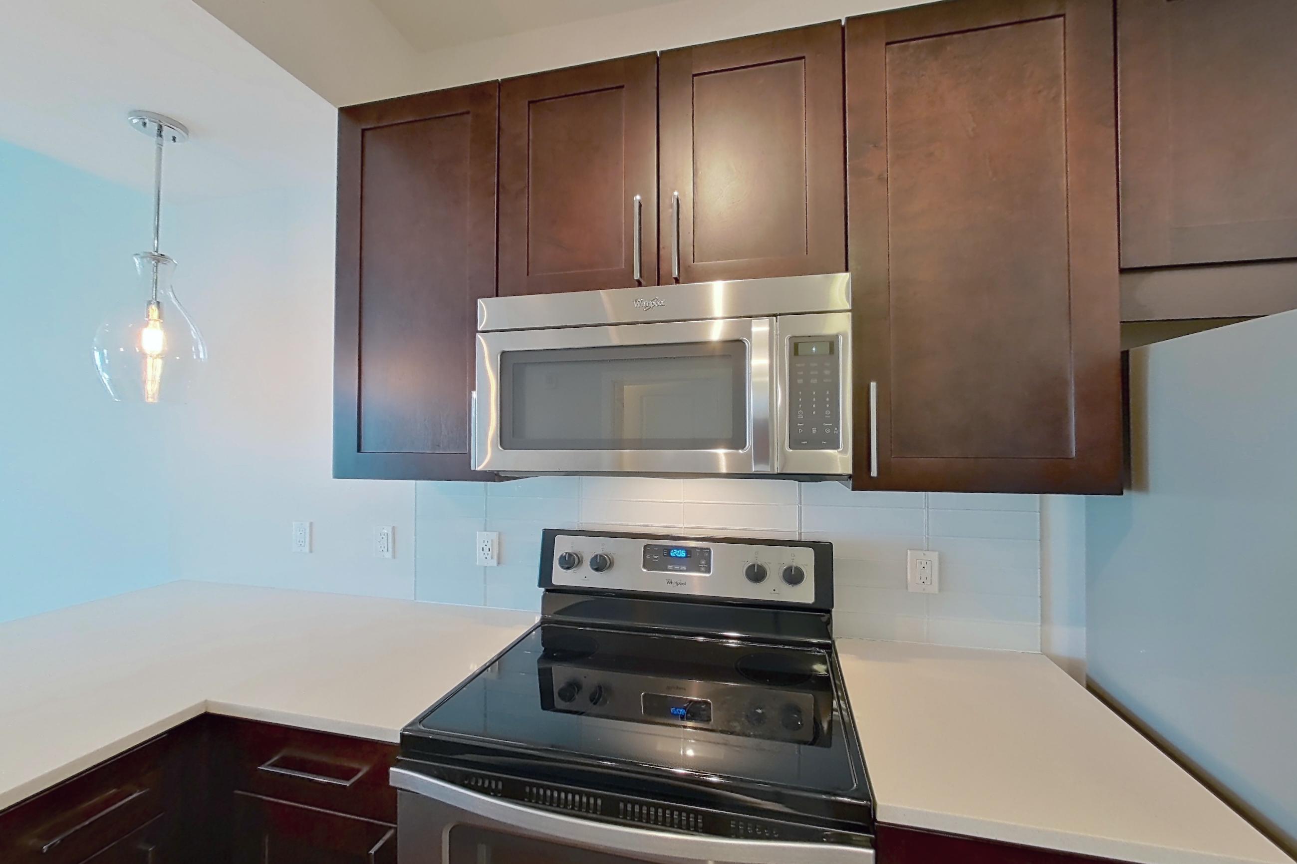 Kitchen with dark wood-finish flooring, dishwasher, electric range, light countertops, microwave, oven/range, refrigerator, stainless steel appliances, and water & ice dispenser, Apartment 1011 at Cyan on Peachtree