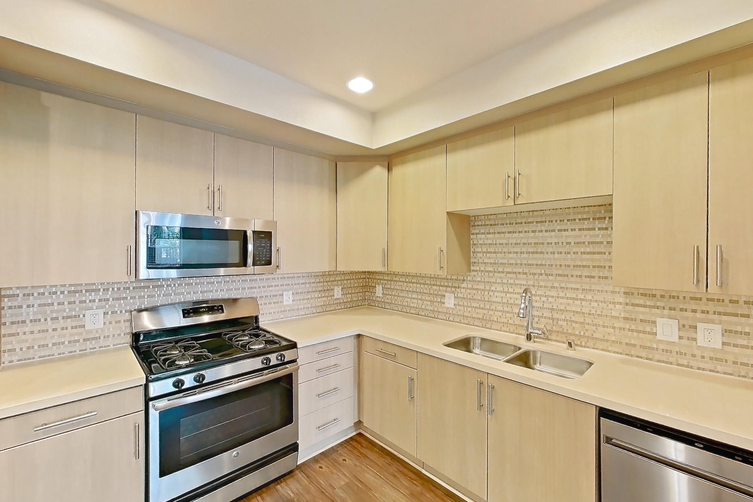 Kitchen with dishwasher, electric range, gas range, light countertops, light wood-finish flooring, microwave, oven/range, refrigerator, and stainless steel appliances, Apartment 1141 at The Verge Apartments