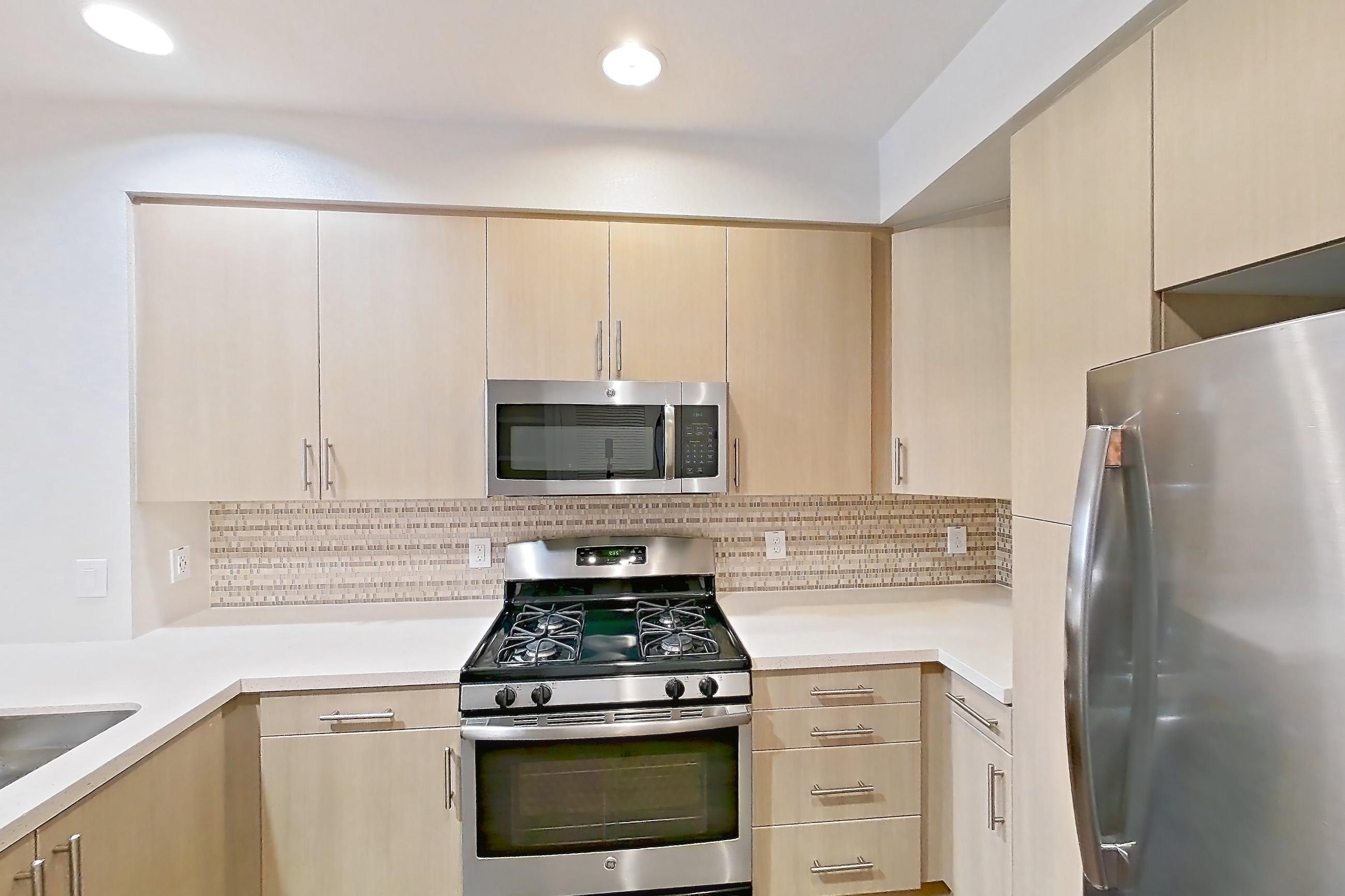 Kitchen with dark wood-finish flooring, dishwasher, gas range, light countertops, light wood-finish flooring, microwave, oven/range, refrigerator, and stainless steel appliances, Apartment 2576 at The Verge Apartments