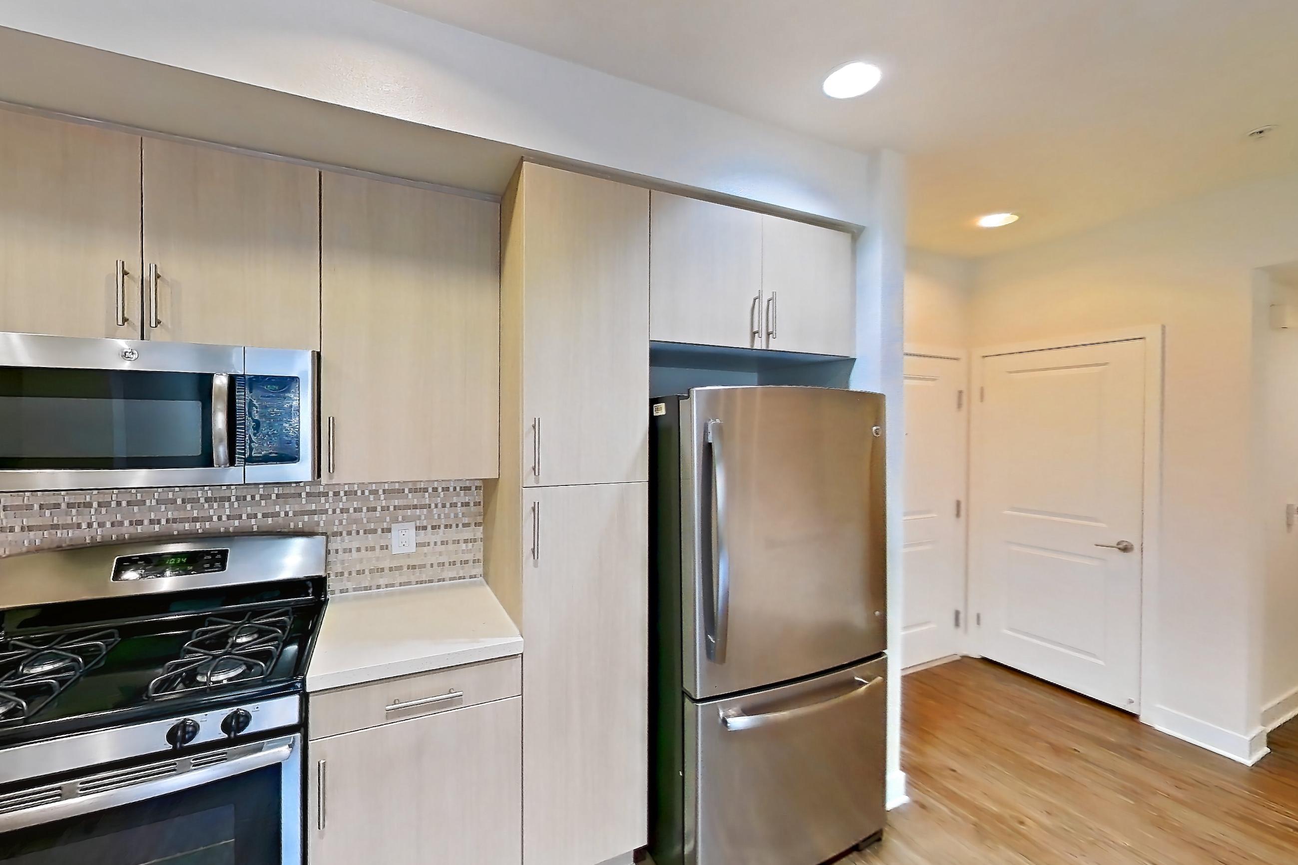 Kitchen with black appliances, dishwasher, gas range, light countertops, light wood-finish flooring, microwave, oven/range, refrigerator, and stainless steel appliances, Apartment 2580 at The Verge Apartments