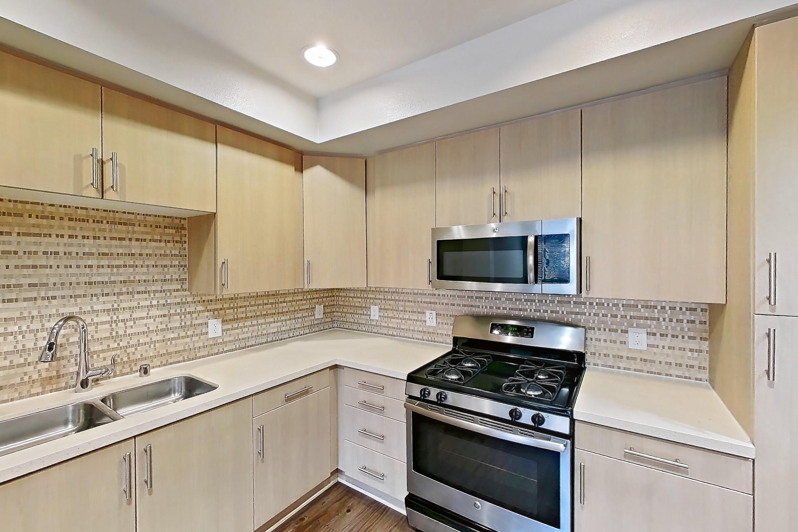 Kitchen with black appliances, dishwasher, gas range, light countertops, light wood-finish flooring, microwave, oven/range, refrigerator, and stainless steel appliances, Apartment 2580 at The Verge Apartments