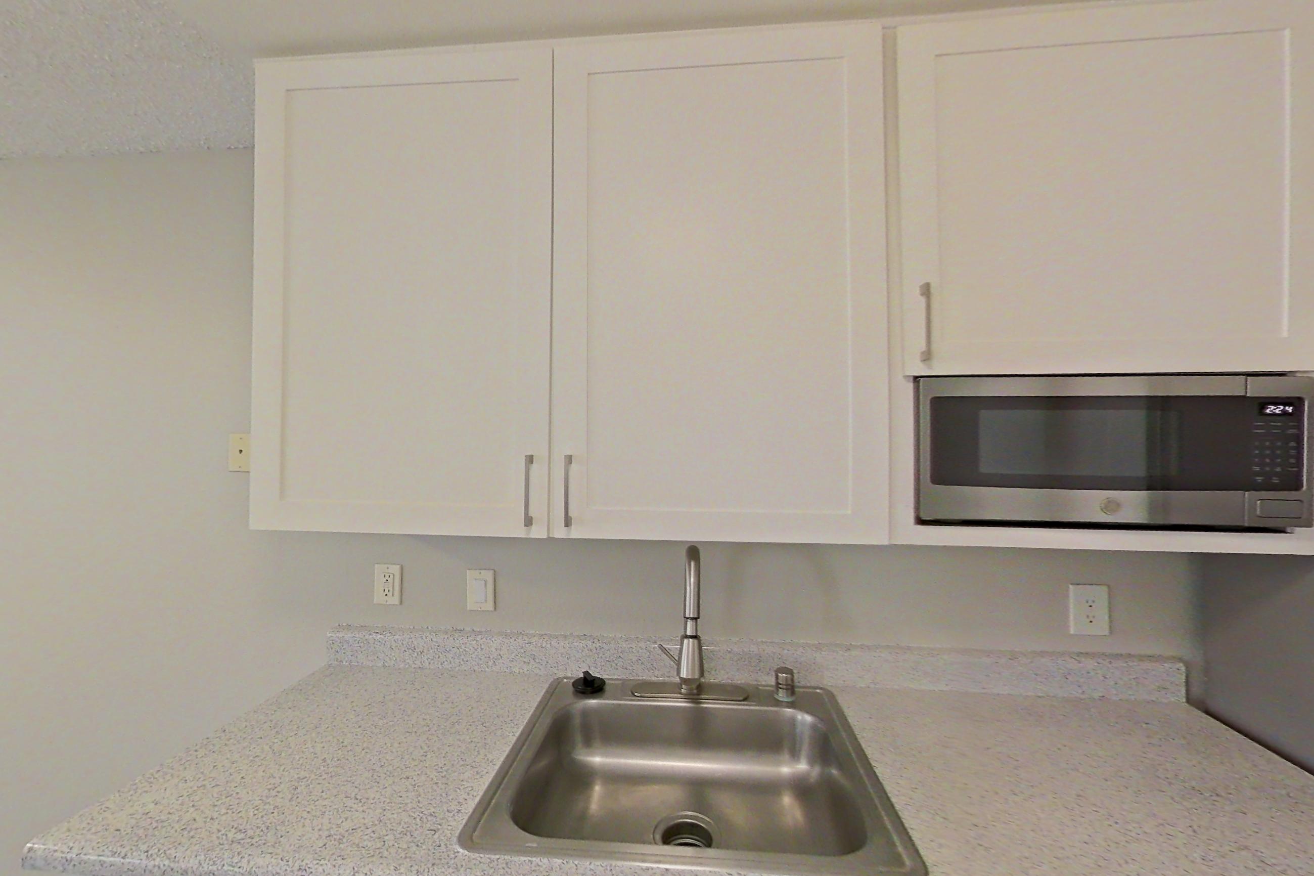 Kitchen with dishwasher, electric range, light countertops, light stone countertops, light wood-finish flooring, microwave, oven/range, refrigerator, stainless steel appliances, and white appliances, Apartment 01-05 at Avana Rancho Cucamonga