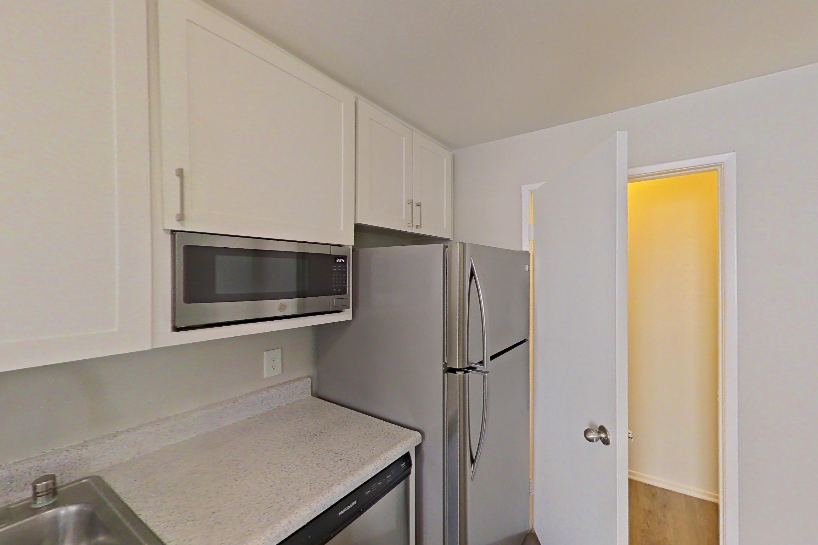 Kitchen with dishwasher, electric range, light countertops, light stone countertops, light wood-finish flooring, microwave, oven/range, refrigerator, stainless steel appliances, and white appliances, Apartment 01-05 at Avana Rancho Cucamonga
