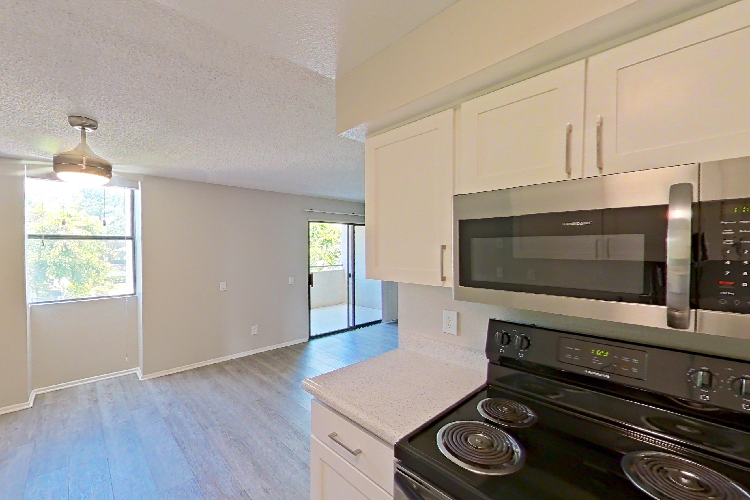 Kitchen with dishwasher, electric range, light stone countertops, light wood-finish flooring, microwave, oven/range, refrigerator, and stainless steel appliances, Apartment 02-07 at Avana Rancho Cucamonga