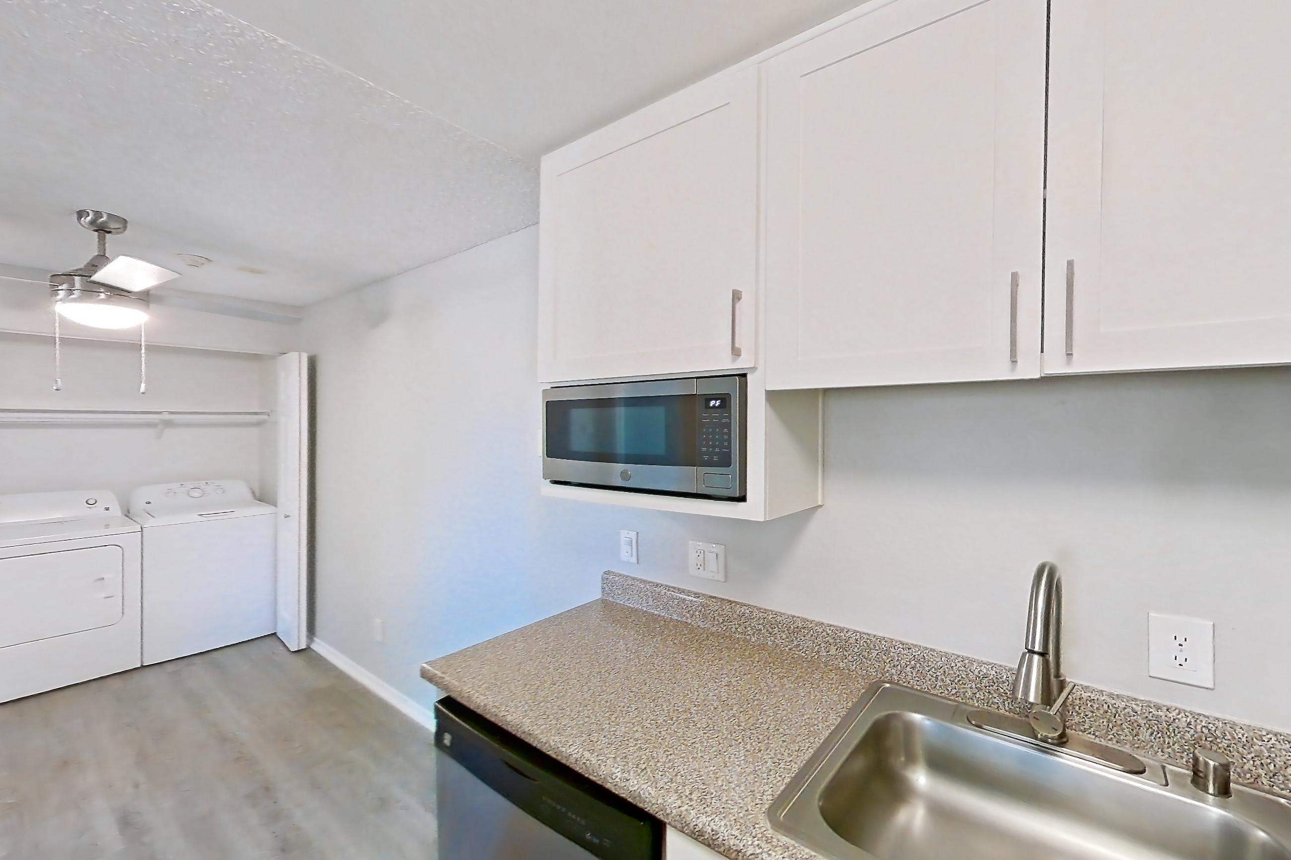 Kitchen with dishwasher, electric range, in-unit laundry, light countertops, light stone countertops, light wood-finish flooring, oven/range, refrigerator, and stainless steel appliances, Apartment 03-09 at Avana Rancho Cucamonga