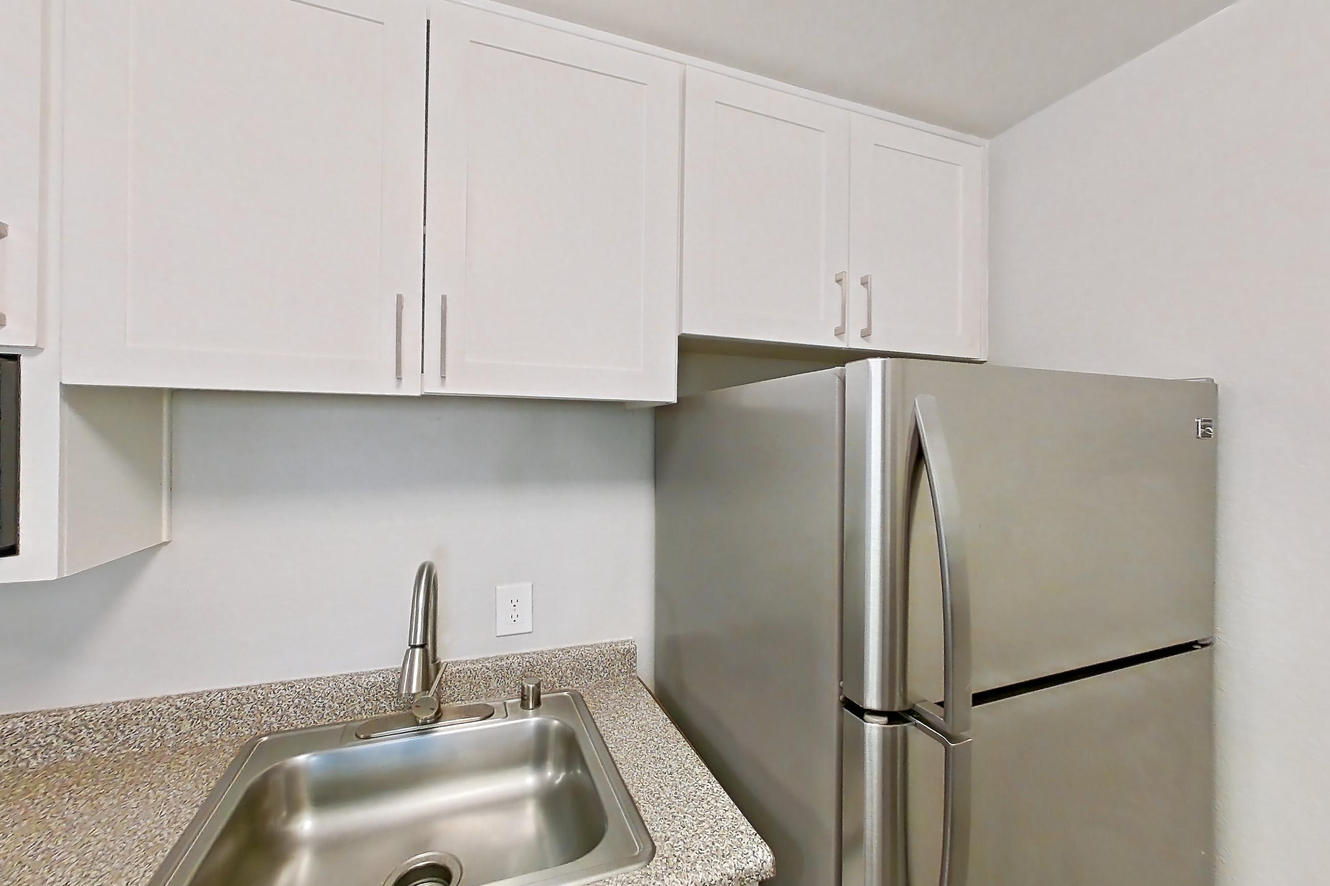 Kitchen with dishwasher, electric range, in-unit laundry, light countertops, light stone countertops, light wood-finish flooring, oven/range, refrigerator, and stainless steel appliances, Apartment 03-09 at Avana Rancho Cucamonga