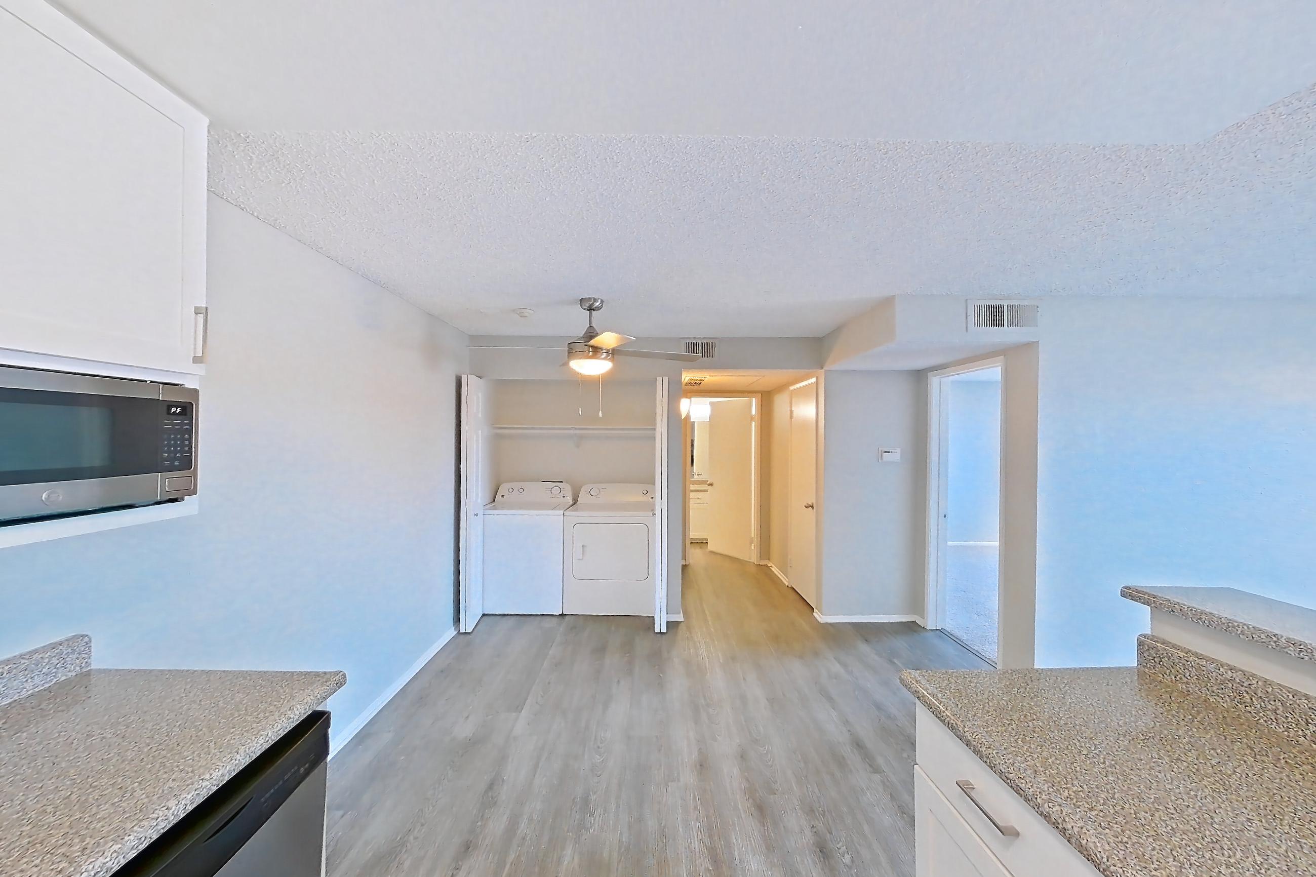 Kitchen with dishwasher, electric range, in-unit laundry, light countertops, light stone countertops, light wood-finish flooring, oven/range, refrigerator, and stainless steel appliances, Apartment 03-10 at Avana Rancho Cucamonga