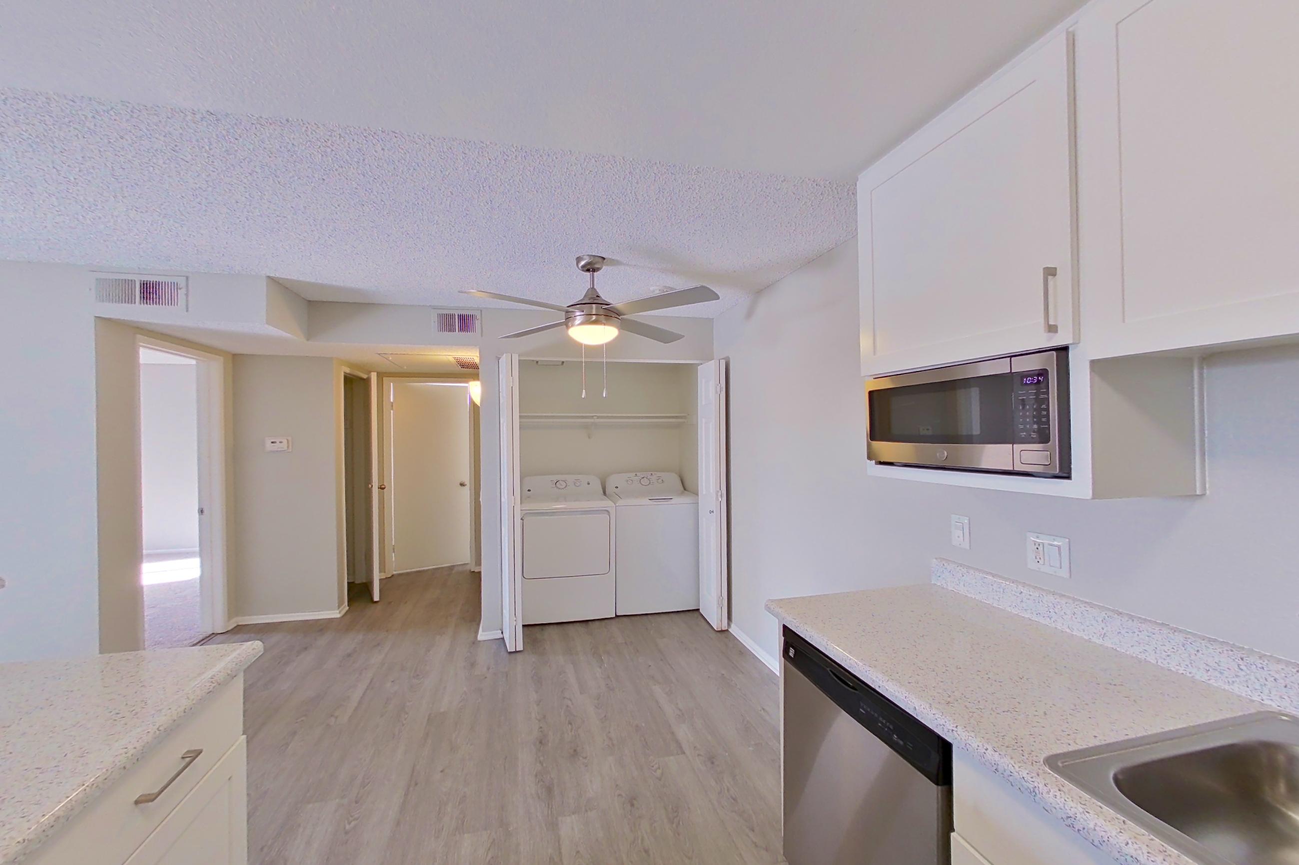 Kitchen with dishwasher, electric range, in-unit laundry, light countertops, light stone countertops, light wood-finish flooring, oven/range, refrigerator, and stainless steel appliances, Apartment 04-05 at Avana Rancho Cucamonga