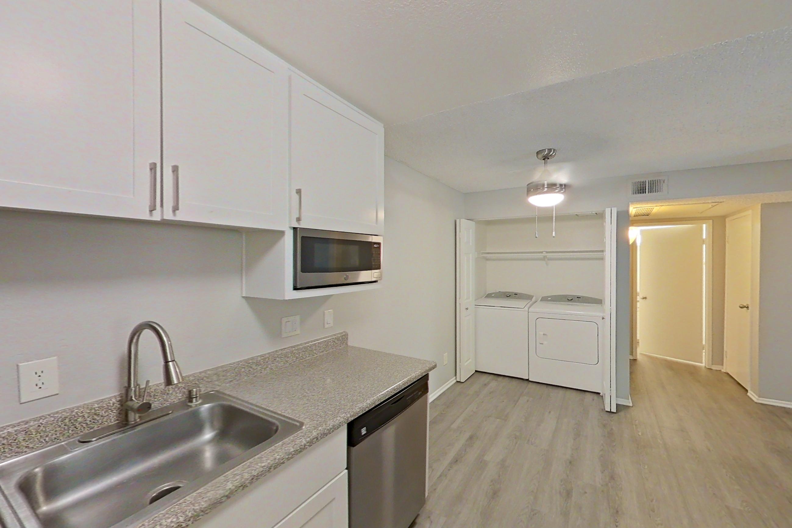 Kitchen with dishwasher, electric range, in-unit laundry, light countertops, light stone countertops, light wood-finish flooring, microwave, oven/range, refrigerator, and stainless steel appliances, Apartment 04-06 at Avana Rancho Cucamonga