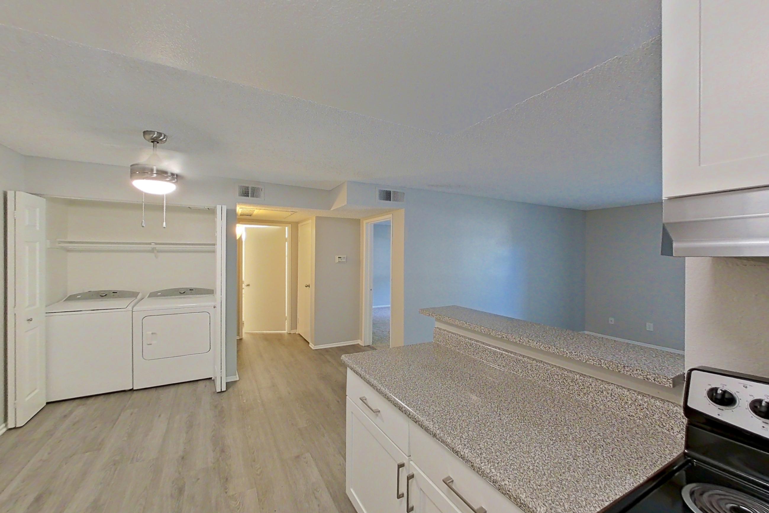 Kitchen with dishwasher, electric range, in-unit laundry, light countertops, light stone countertops, light wood-finish flooring, microwave, oven/range, refrigerator, and stainless steel appliances, Apartment 04-06 at Avana Rancho Cucamonga