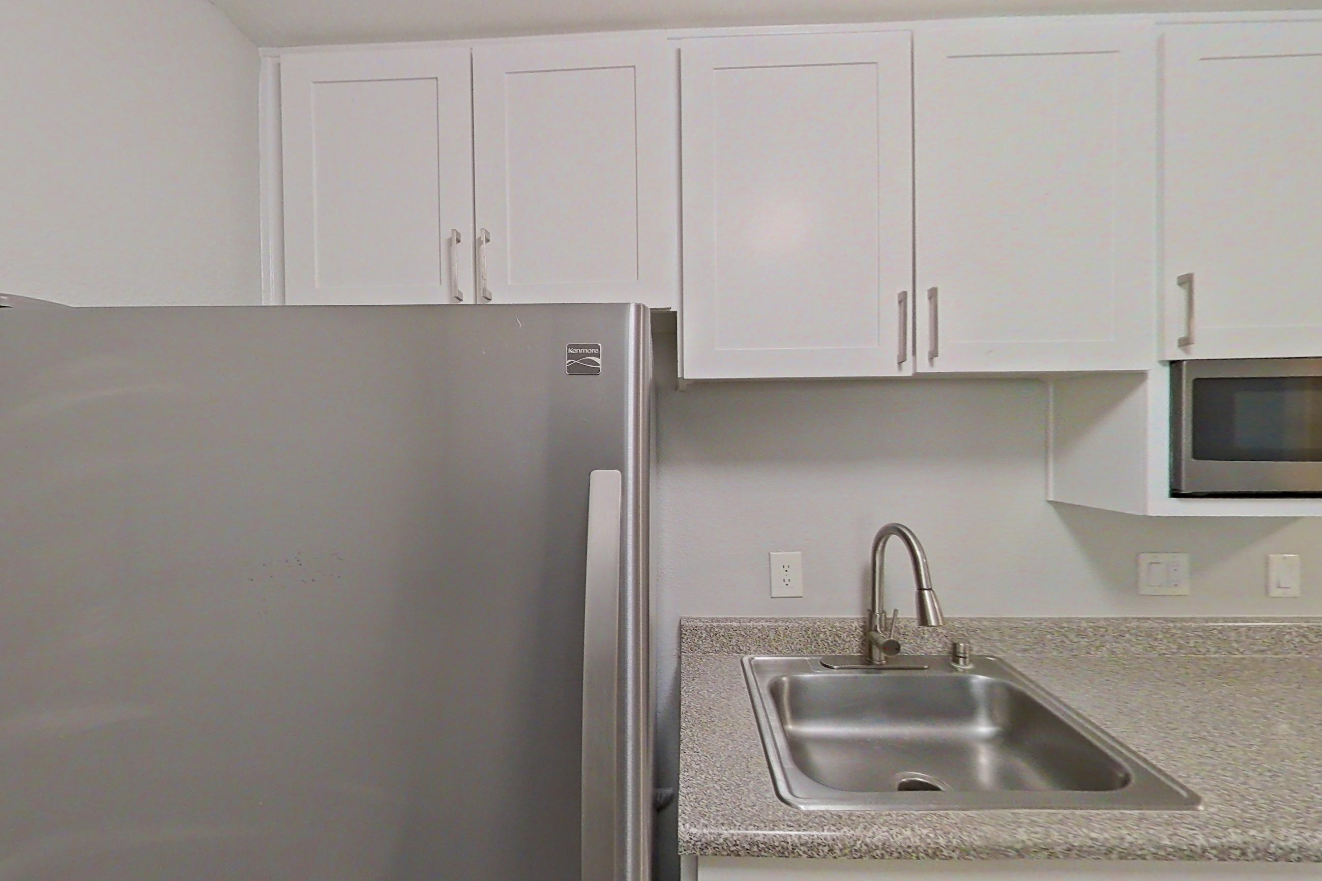 Kitchen with dishwasher, electric range, in-unit laundry, light countertops, light stone countertops, light wood-finish flooring, microwave, oven/range, refrigerator, and stainless steel appliances, Apartment 04-06 at Avana Rancho Cucamonga
