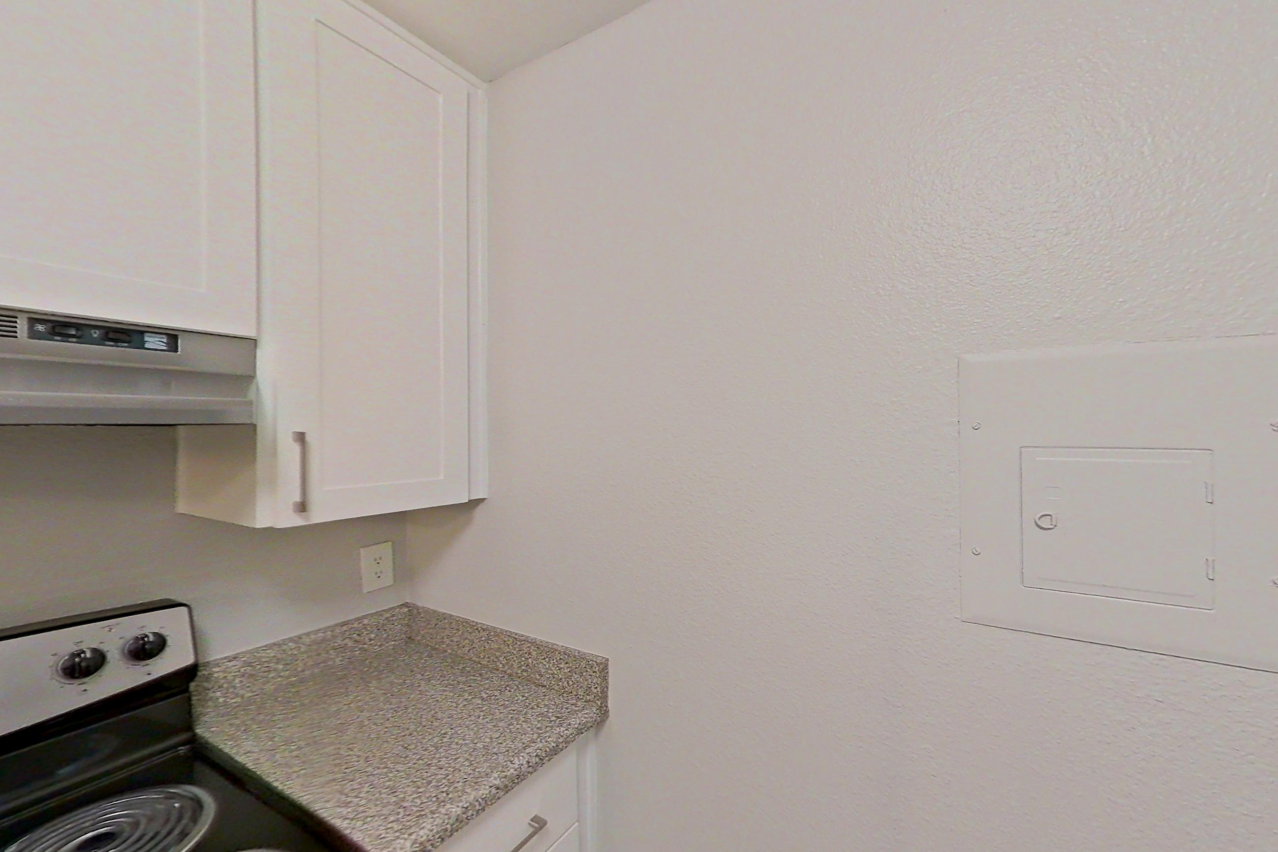 Kitchen with dishwasher, electric range, in-unit laundry, light countertops, light stone countertops, light wood-finish flooring, microwave, oven/range, refrigerator, and stainless steel appliances, Apartment 04-06 at Avana Rancho Cucamonga