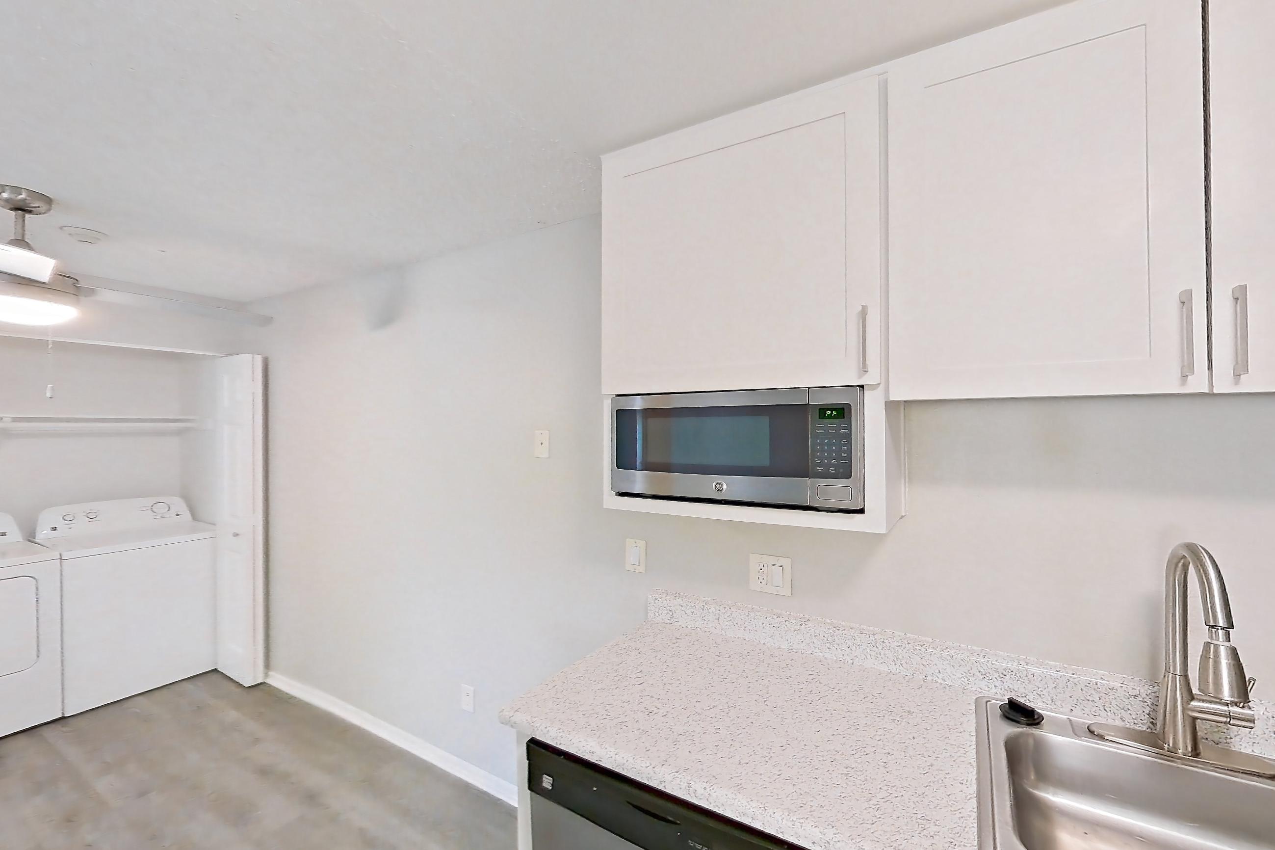 Kitchen with black appliances, dishwasher, electric range, in-unit laundry, light countertops, light stone countertops, light wood-finish flooring, microwave, oven/range, and stainless steel appliances, Apartment 04-08 at Avana Rancho Cucamonga