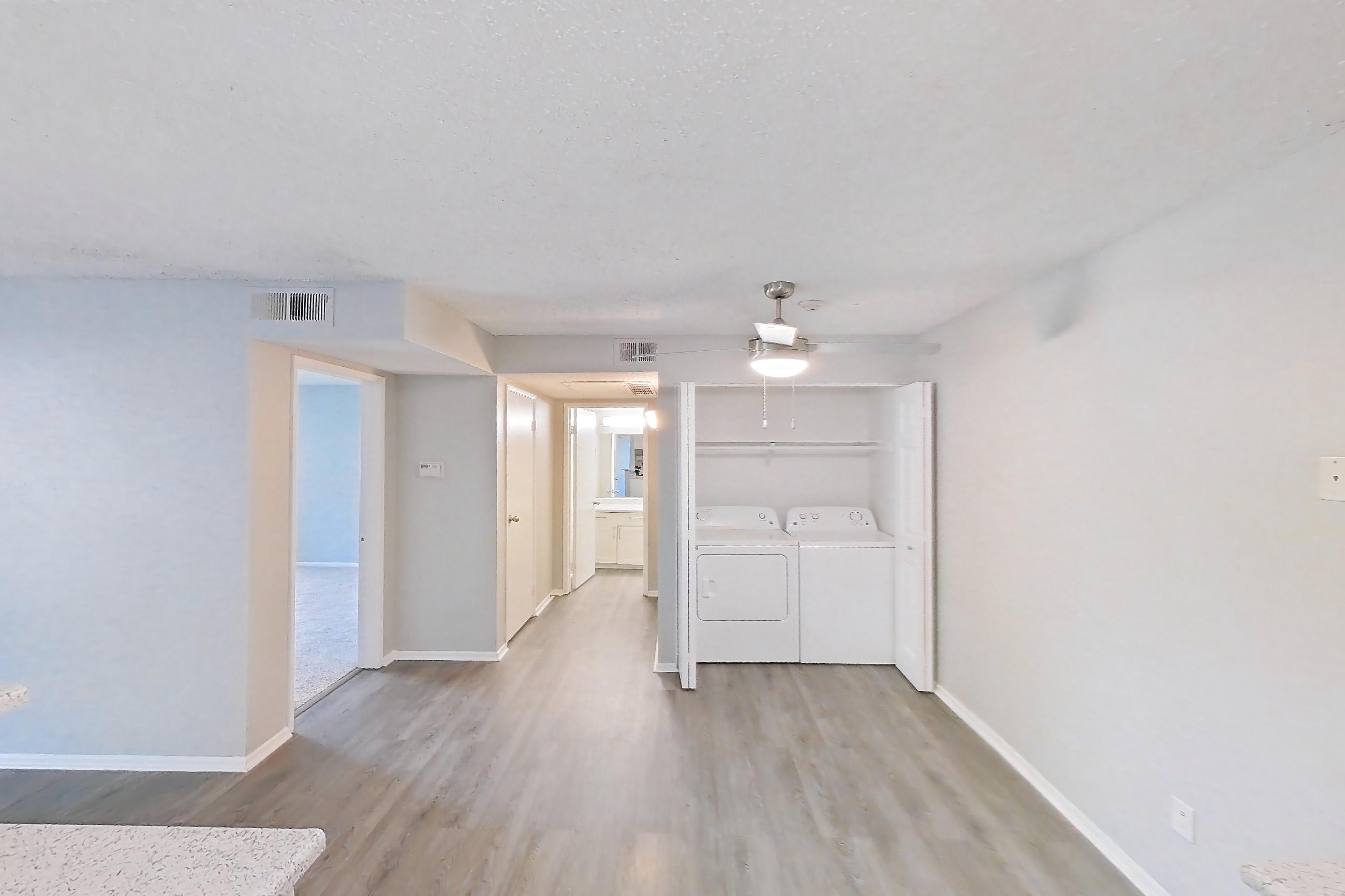 Kitchen with black appliances, dishwasher, electric range, in-unit laundry, light countertops, light stone countertops, light wood-finish flooring, microwave, oven/range, and stainless steel appliances, Apartment 04-08 at Avana Rancho Cucamonga