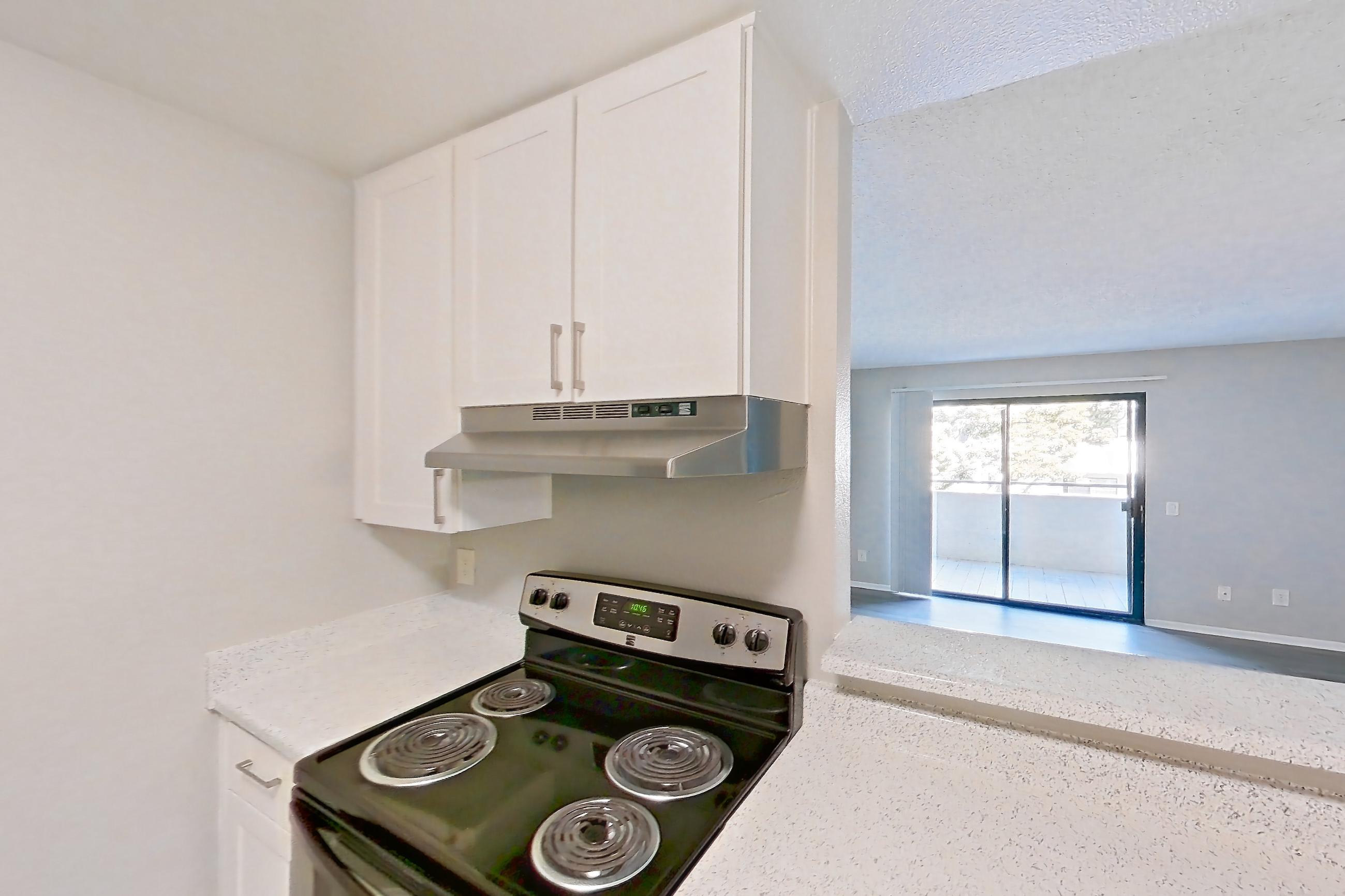 Kitchen with black appliances, dishwasher, electric range, in-unit laundry, light countertops, light stone countertops, light wood-finish flooring, microwave, oven/range, and stainless steel appliances, Apartment 04-08 at Avana Rancho Cucamonga