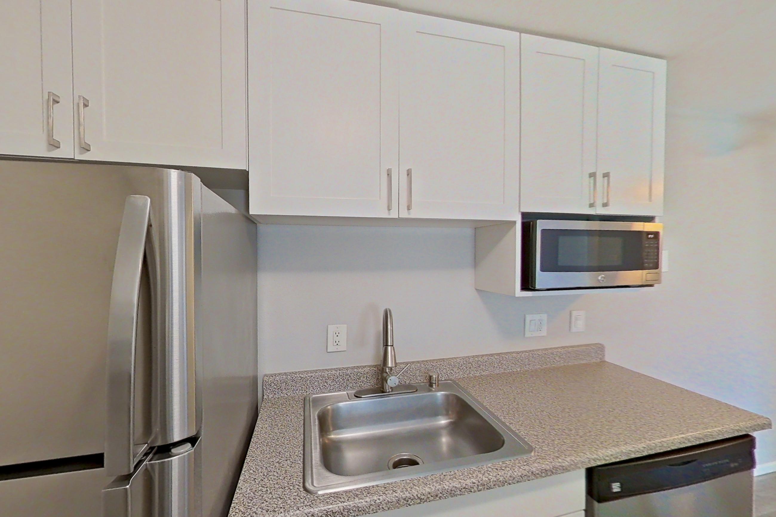 Kitchen with dishwasher, electric range, in-unit laundry, light countertops, light stone countertops, light wood-finish flooring, oven/range, and stainless steel appliances, Apartment 05-03 at Avana Rancho Cucamonga