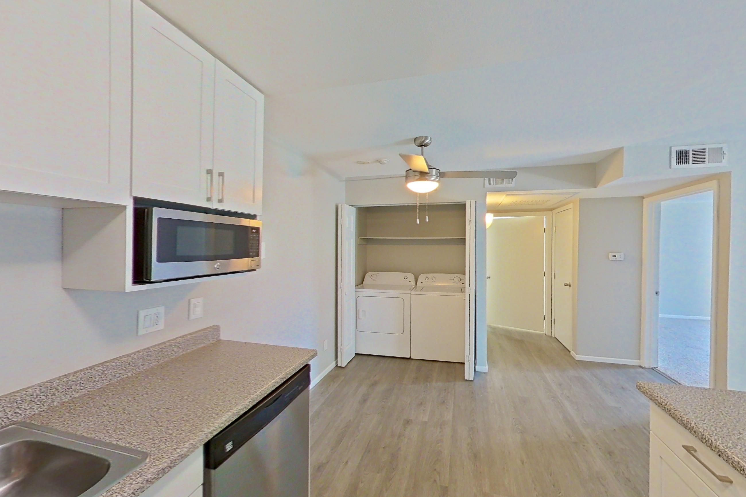 Kitchen with dishwasher, electric range, in-unit laundry, light countertops, light stone countertops, light wood-finish flooring, oven/range, and stainless steel appliances, Apartment 05-03 at Avana Rancho Cucamonga