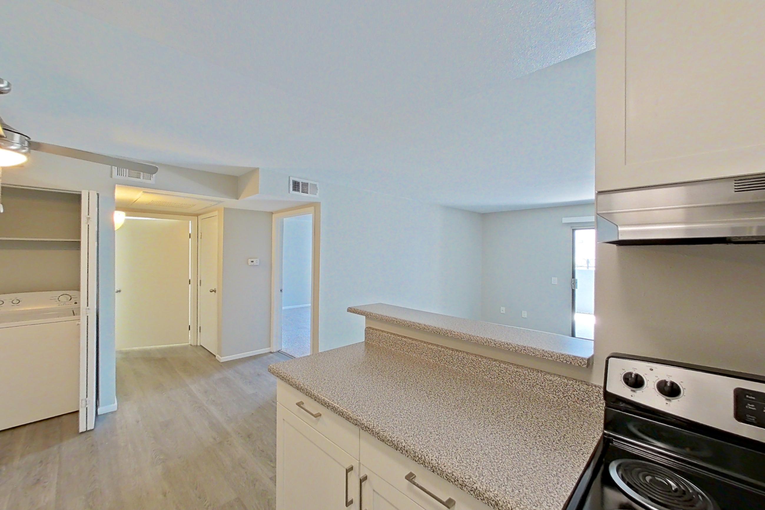 Kitchen with dishwasher, electric range, in-unit laundry, light countertops, light stone countertops, light wood-finish flooring, oven/range, and stainless steel appliances, Apartment 05-03 at Avana Rancho Cucamonga
