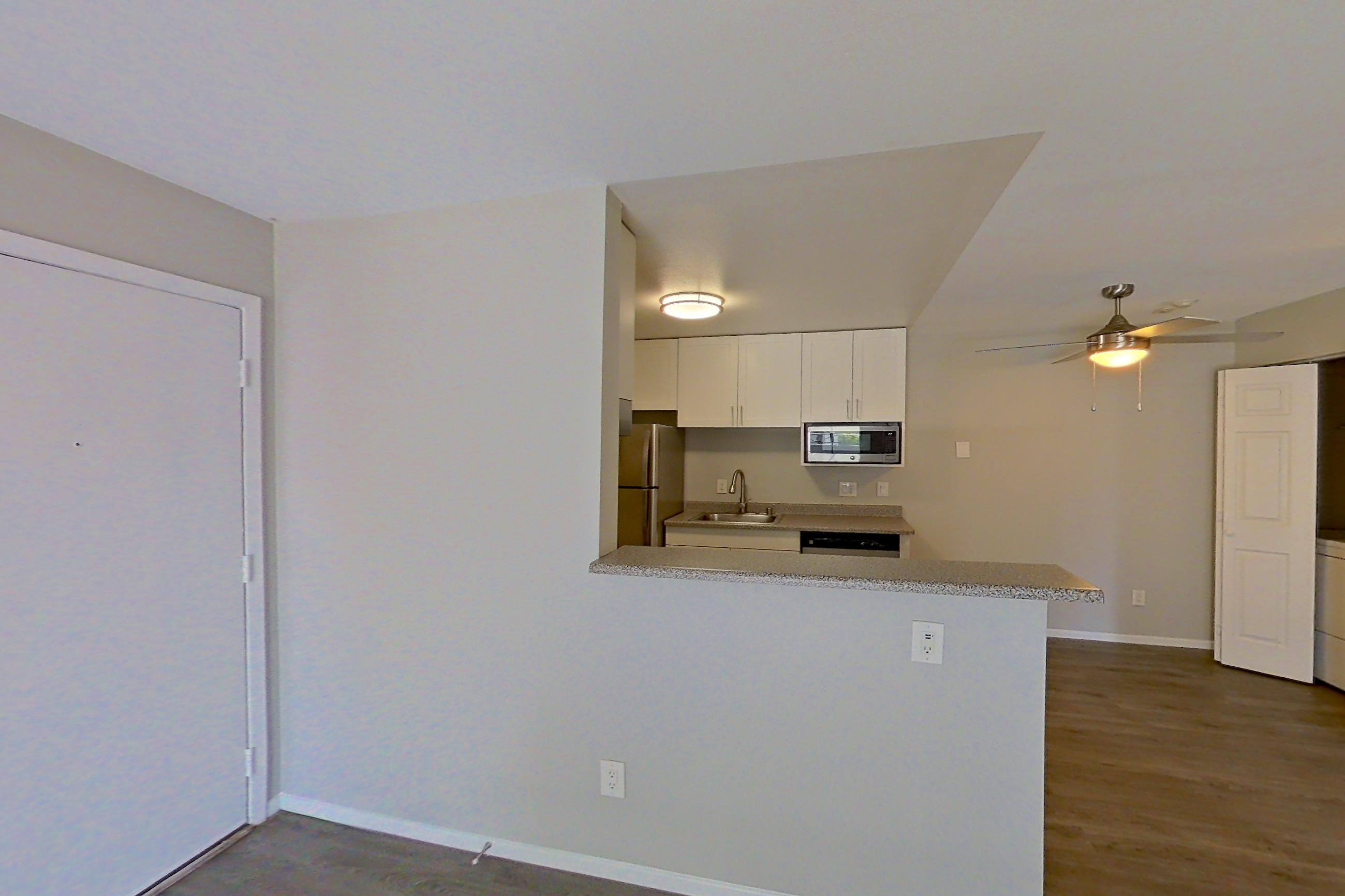 Living room with dark wood-finish flooring, light countertops, refrigerator, and stainless steel appliances, Apartment 05-03 at Avana Rancho Cucamonga