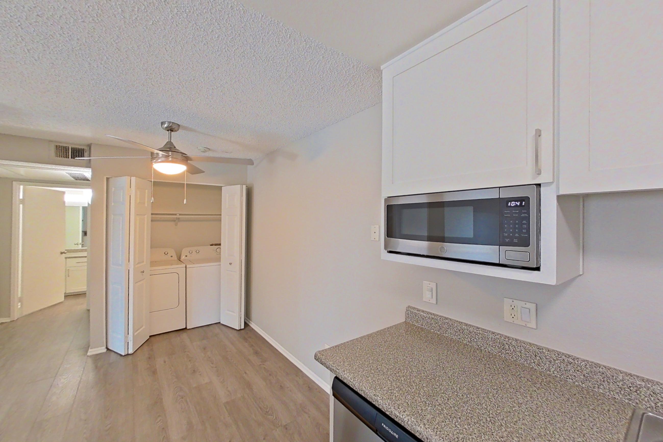 Kitchen with dishwasher, in-unit laundry, light countertops, light stone countertops, light wood-finish flooring, microwave, oven/range, refrigerator, and stainless steel appliances, Apartment 05-05 at Avana Rancho Cucamonga