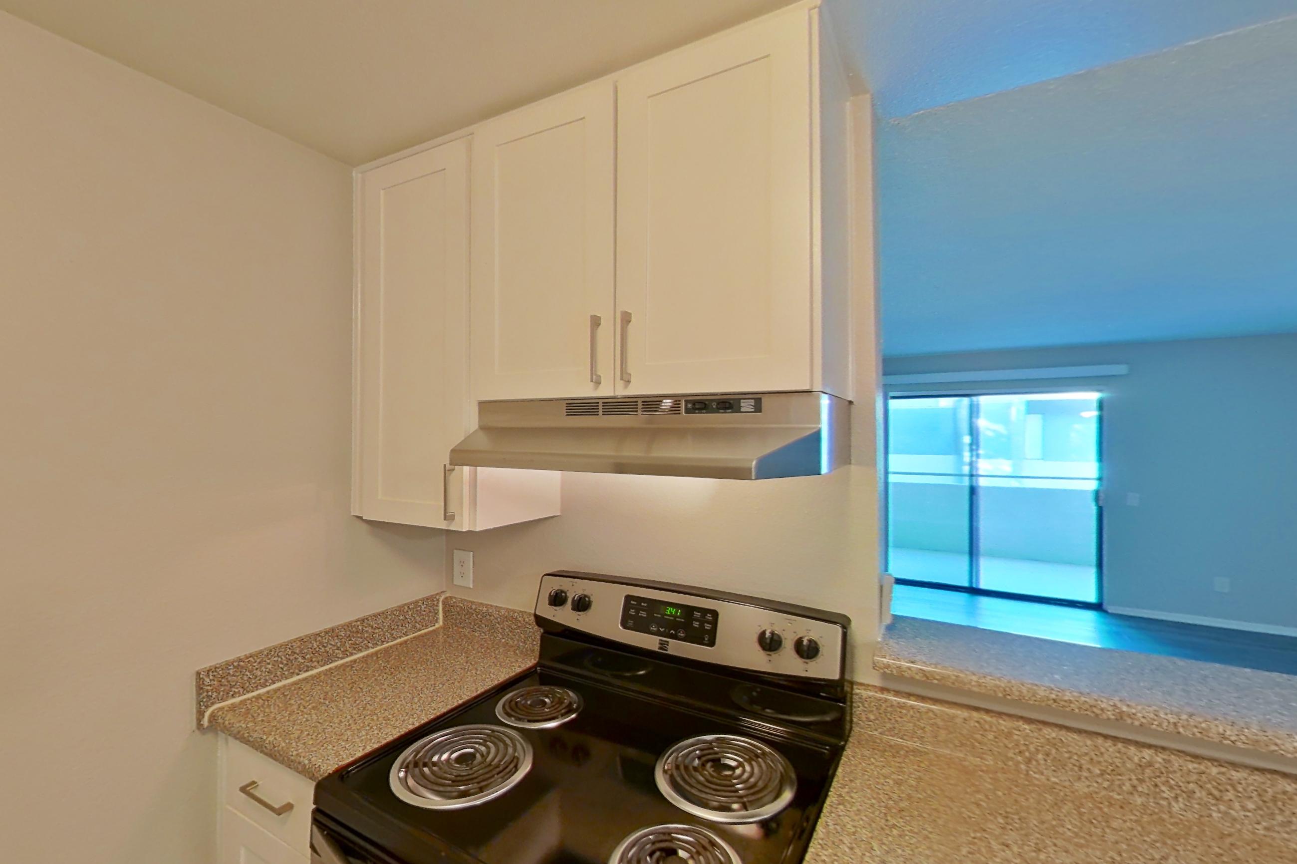 Kitchen with dishwasher, electric range, light countertops, light stone countertops, light wood-finish flooring, microwave, oven/range, refrigerator, and stainless steel appliances, Apartment 05-08 at Avana Rancho Cucamonga