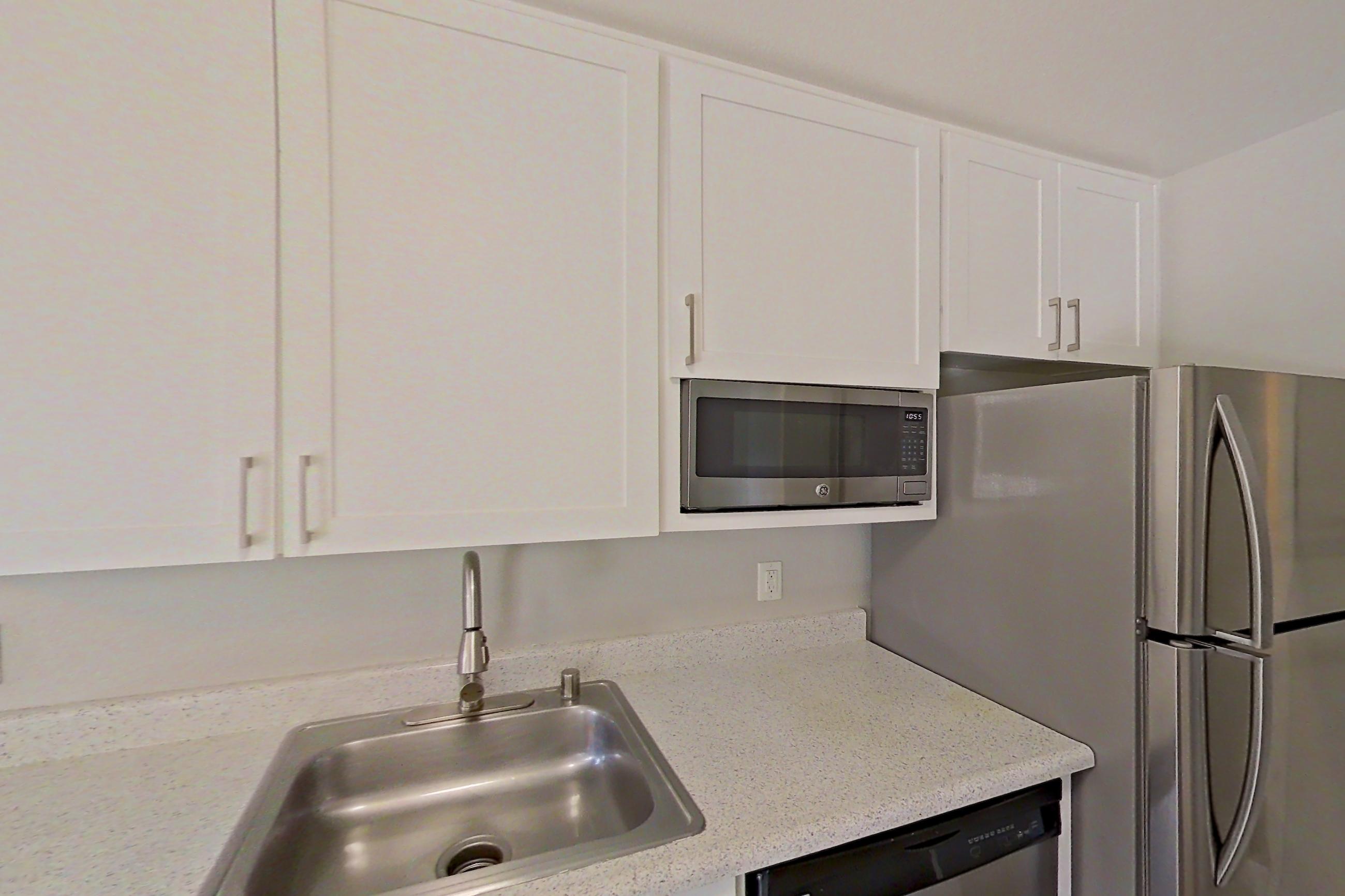 Kitchen with dark wood-finish flooring, dishwasher, electric range, light stone countertops, light wood-finish flooring, oven/range, range hood, and stainless steel appliances, Apartment 06-05 at Avana Rancho Cucamonga