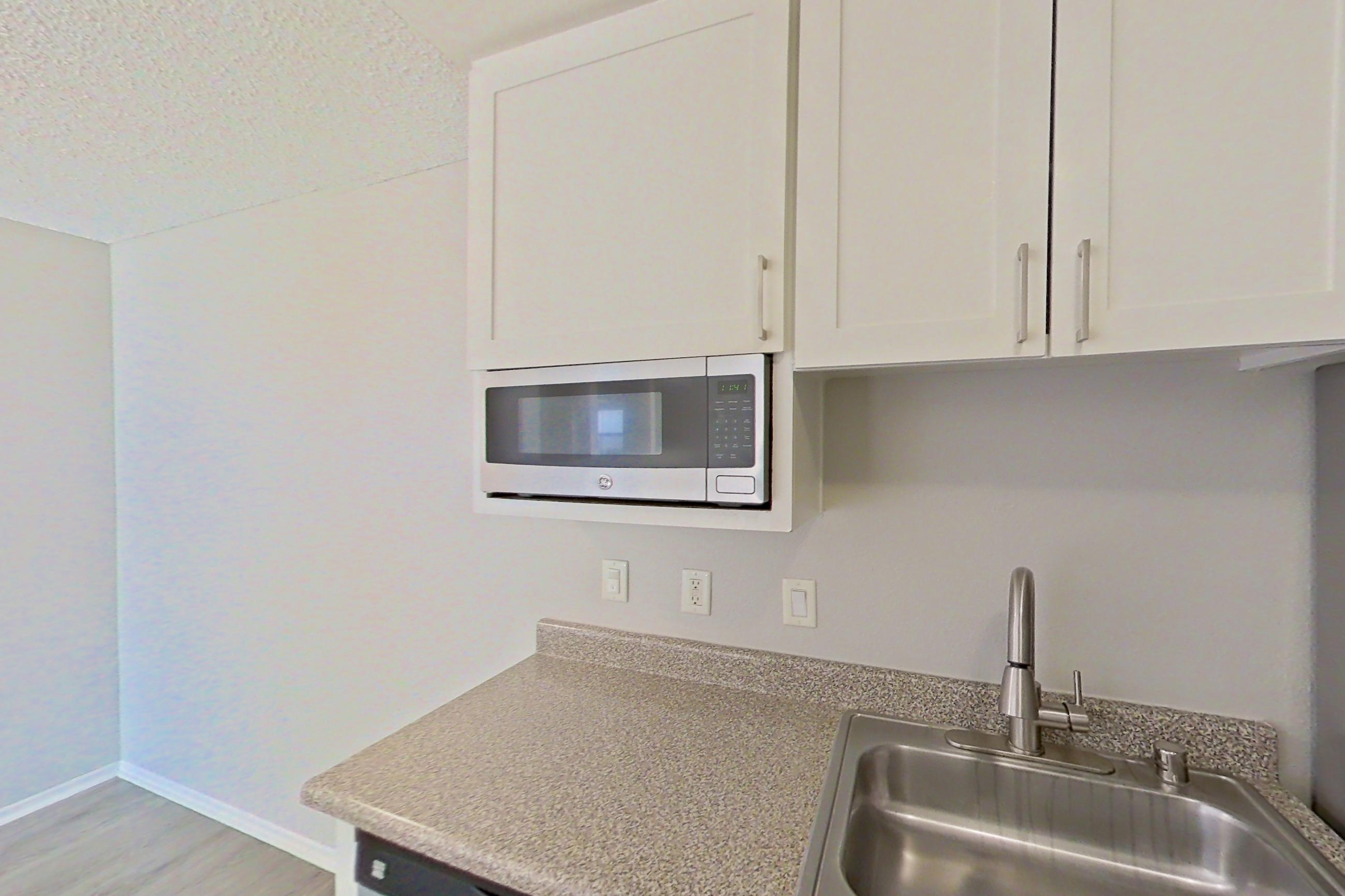 Kitchen with dishwasher, electric range, light countertops, light wood-finish flooring, microwave, oven/range, refrigerator, and stainless steel appliances, Apartment 06-06 at Avana Rancho Cucamonga