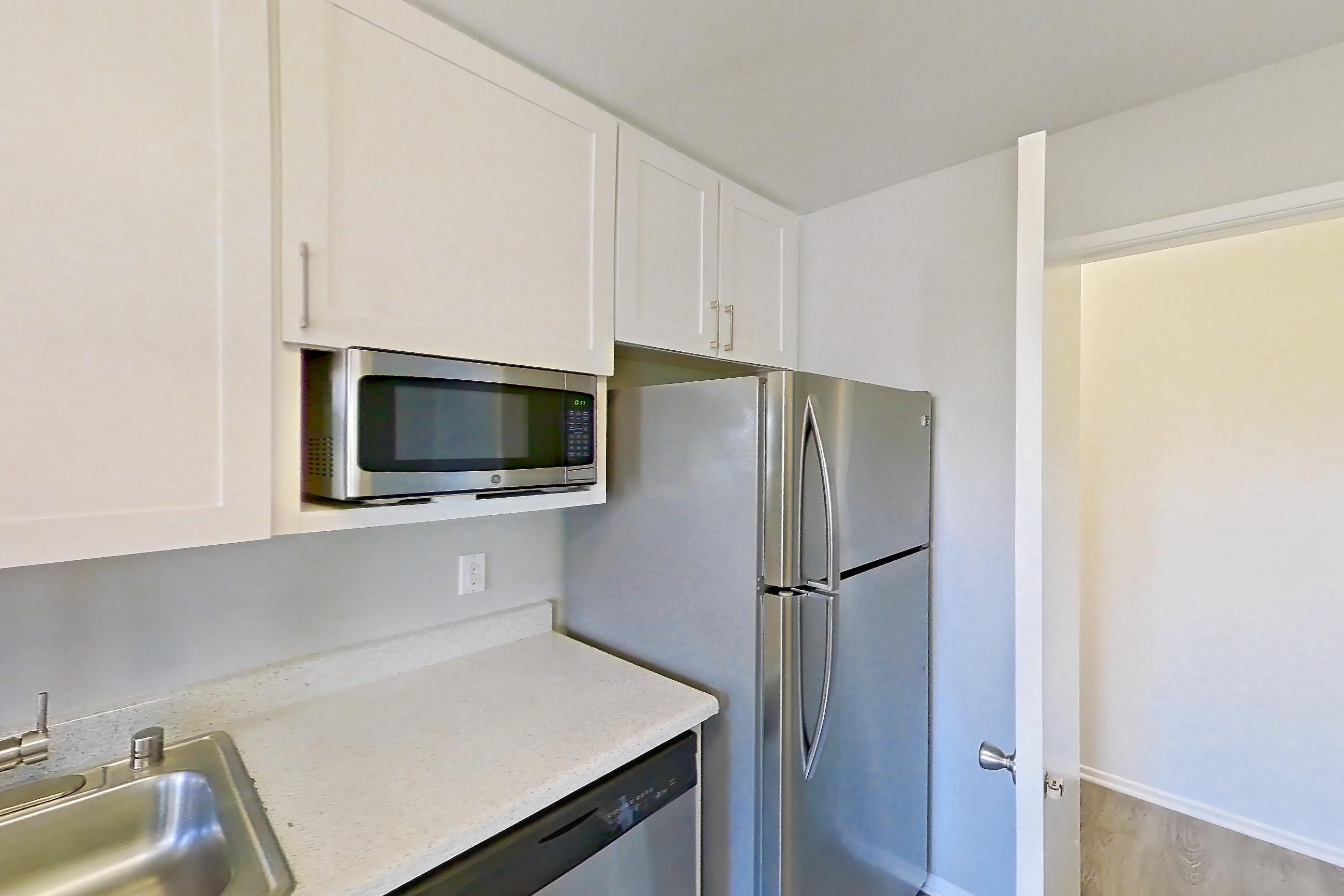 Kitchen with dishwasher, electric range, light countertops, light stone countertops, light wood-finish flooring, microwave, oven/range, range hood, and stainless steel appliances, Apartment 07-01 at Avana Rancho Cucamonga