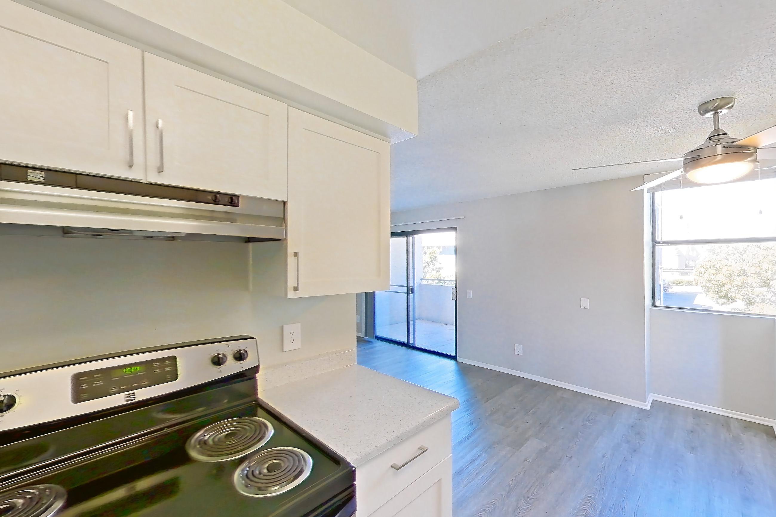 Kitchen with dishwasher, electric range, light countertops, light stone countertops, light wood-finish flooring, microwave, oven/range, range hood, and stainless steel appliances, Apartment 07-01 at Avana Rancho Cucamonga