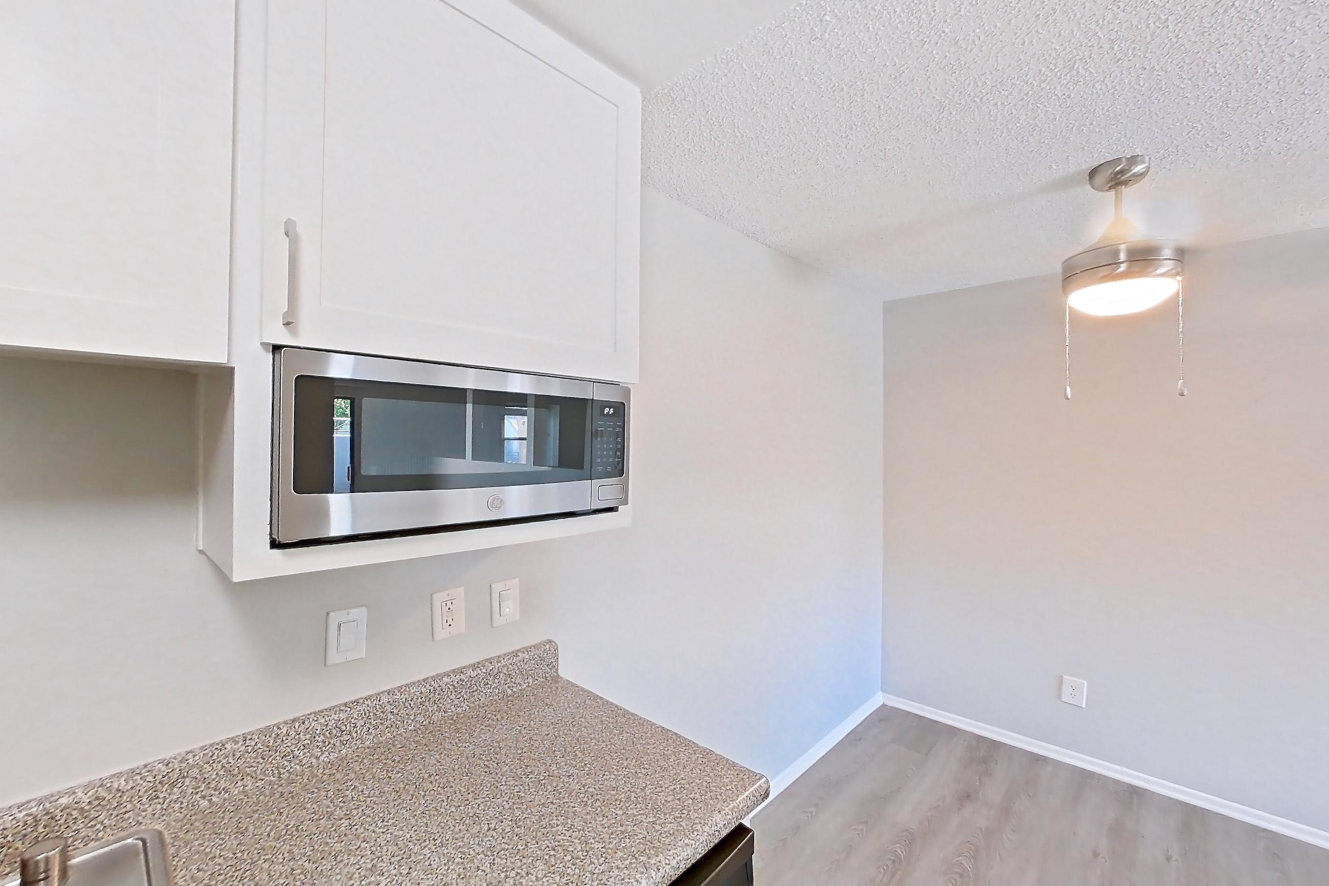 Kitchen with built-in microwave, dishwasher, electric range, light countertops, light stone countertops, light wood-finish flooring, microwave, refrigerator, and stainless steel appliances, Apartment 10-04 at Avana Rancho Cucamonga