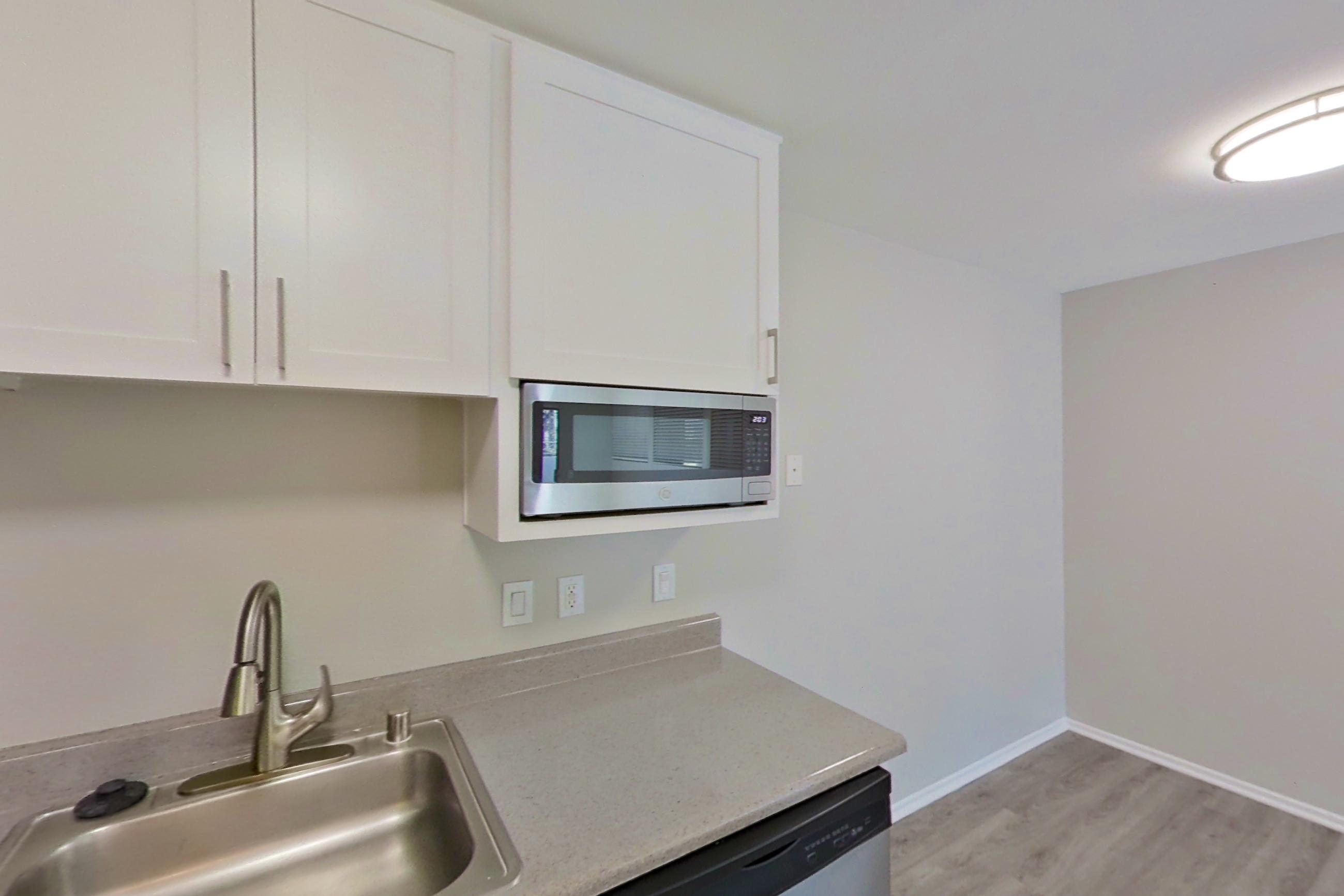 Kitchen with black appliances, dishwasher, electric range, light countertops, light stone countertops, light wood-finish flooring, microwave, oven/range, range hood, refrigerator, stainless steel appliances, and white appliances, Apartment 10-12 at Avana Rancho Cucamonga