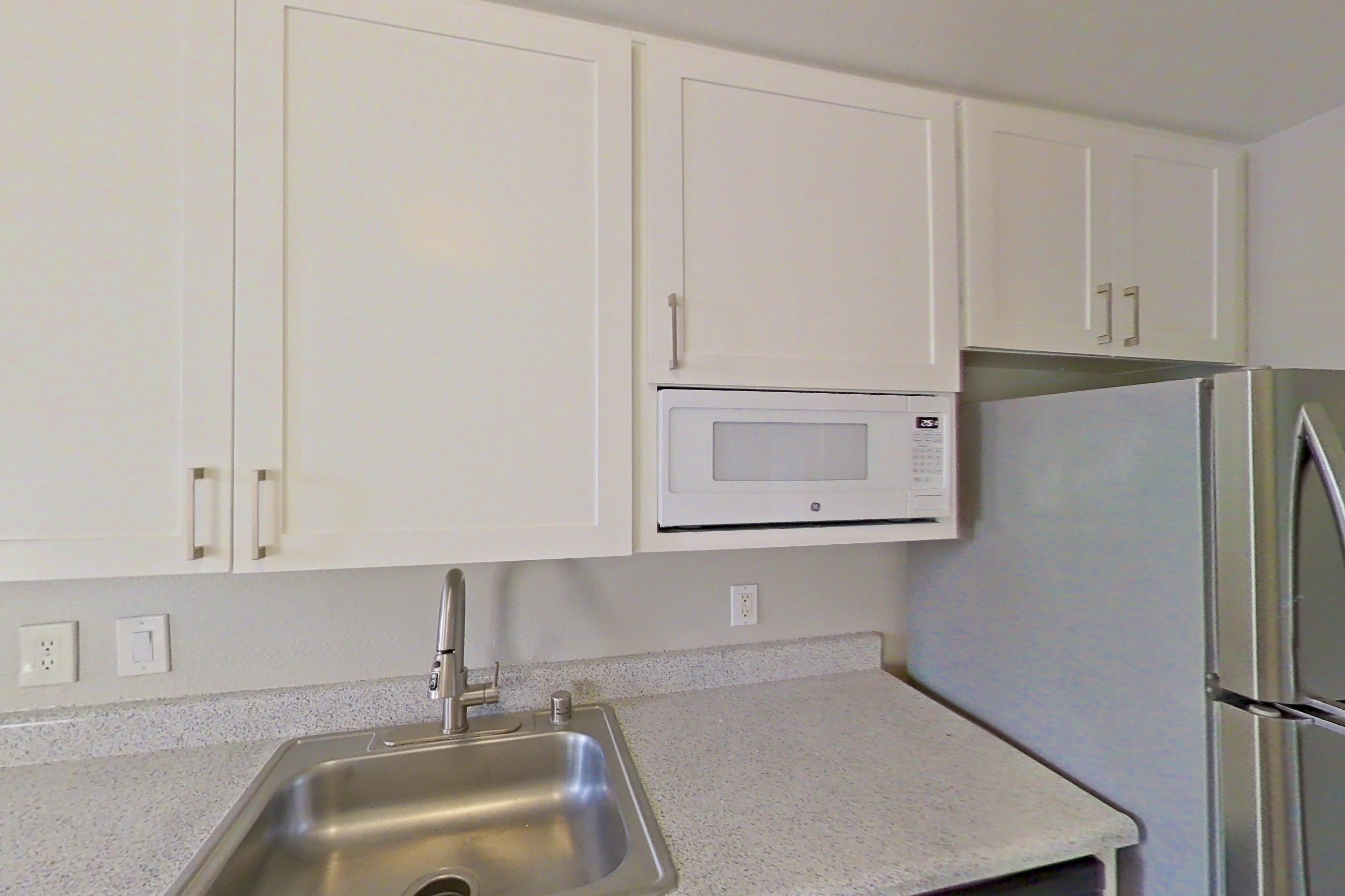 Kitchen with dishwasher, electric range, light countertops, light stone countertops, light wood-finish flooring, oven/range, range hood, refrigerator, and stainless steel appliances, Apartment 11-01 at Avana Rancho Cucamonga