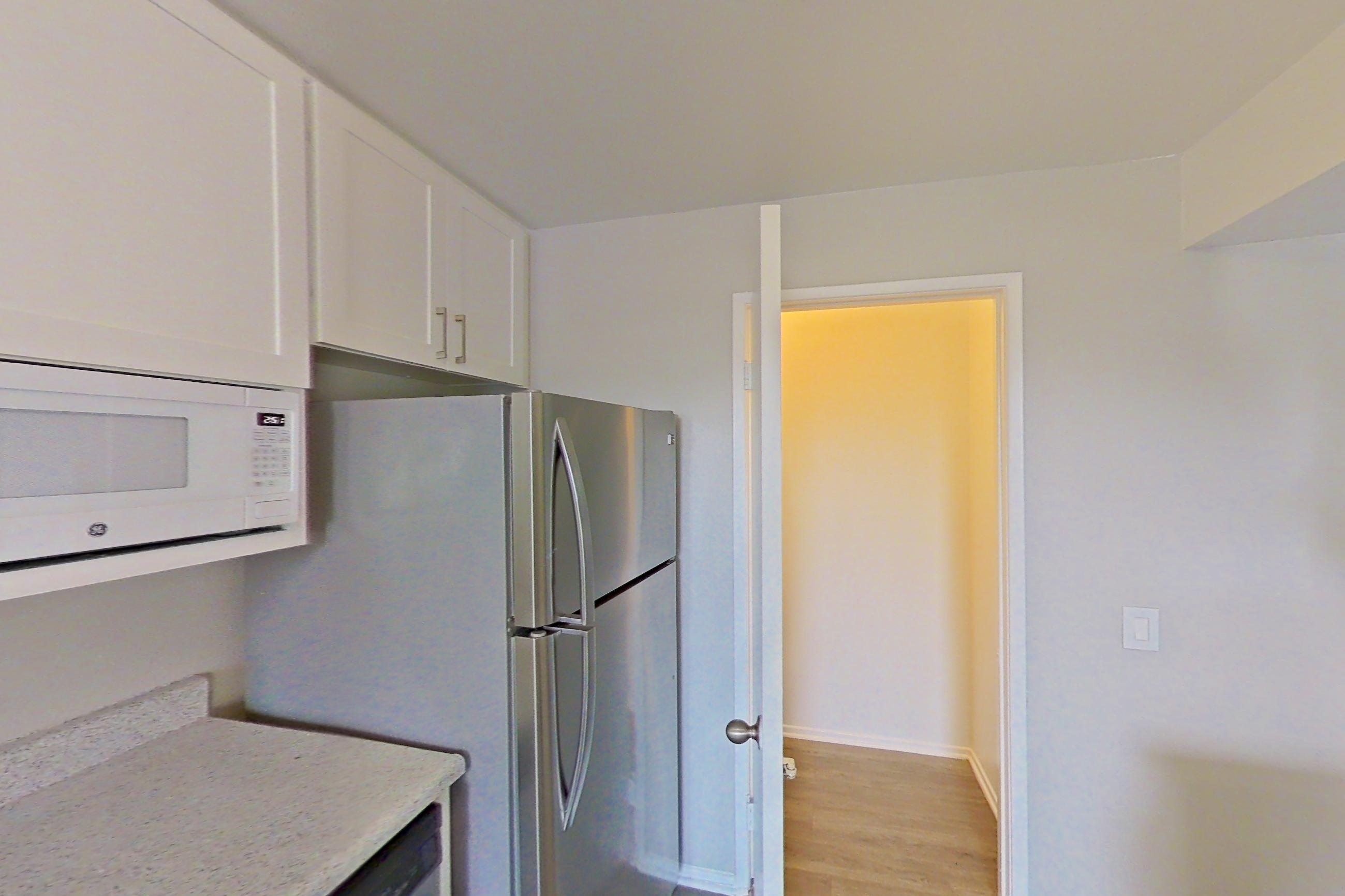 Kitchen with dishwasher, electric range, light countertops, light stone countertops, light wood-finish flooring, oven/range, range hood, refrigerator, and stainless steel appliances, Apartment 11-01 at Avana Rancho Cucamonga