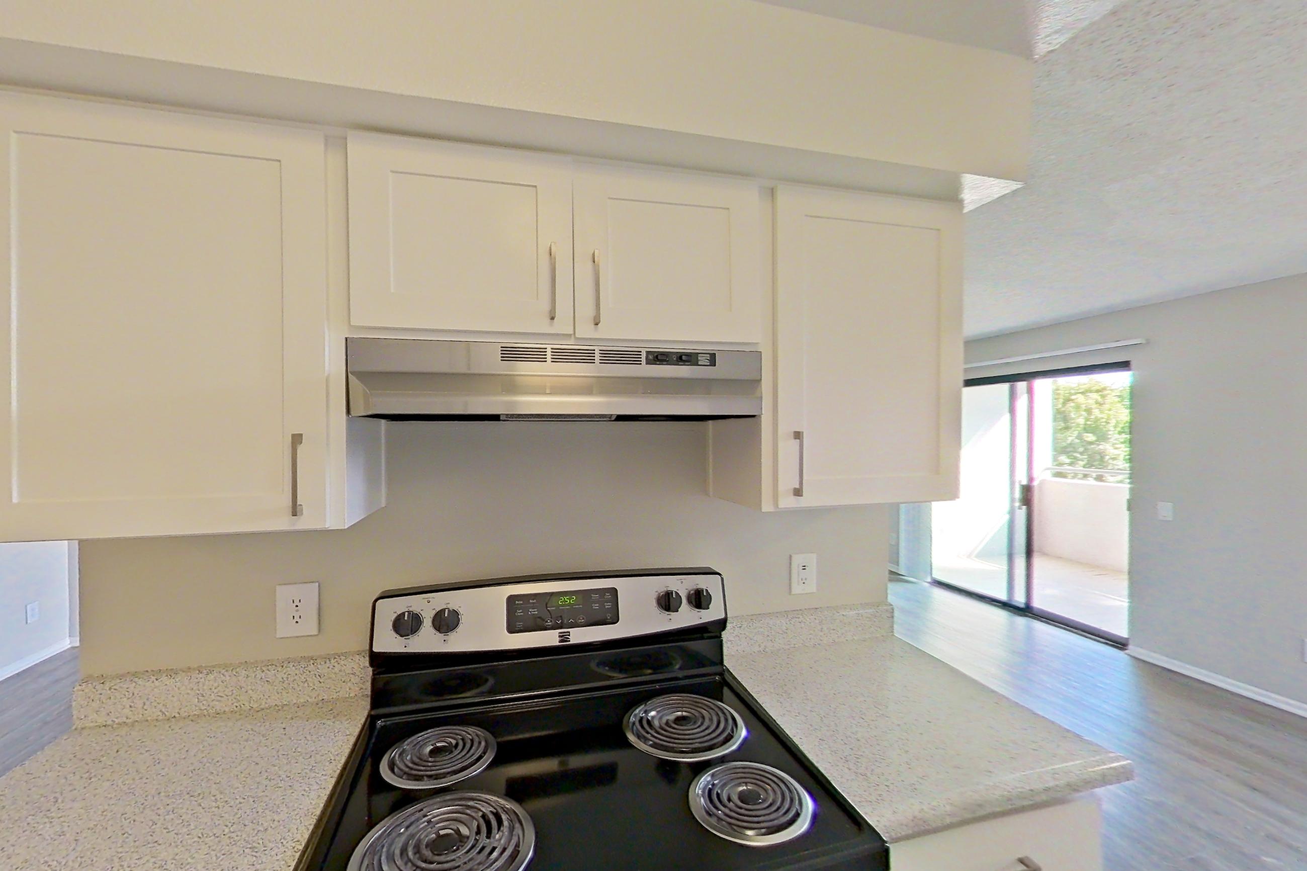 Kitchen with dishwasher, electric range, light countertops, light stone countertops, light wood-finish flooring, oven/range, range hood, refrigerator, and stainless steel appliances, Apartment 11-01 at Avana Rancho Cucamonga